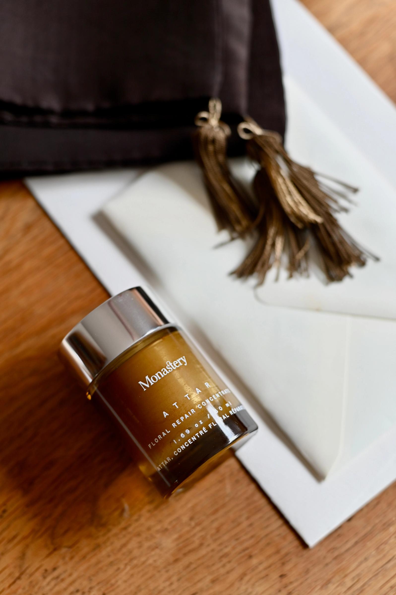 Monastery skincare products displayed, including Attar with silver caps. Arranged on light surface with soft background.