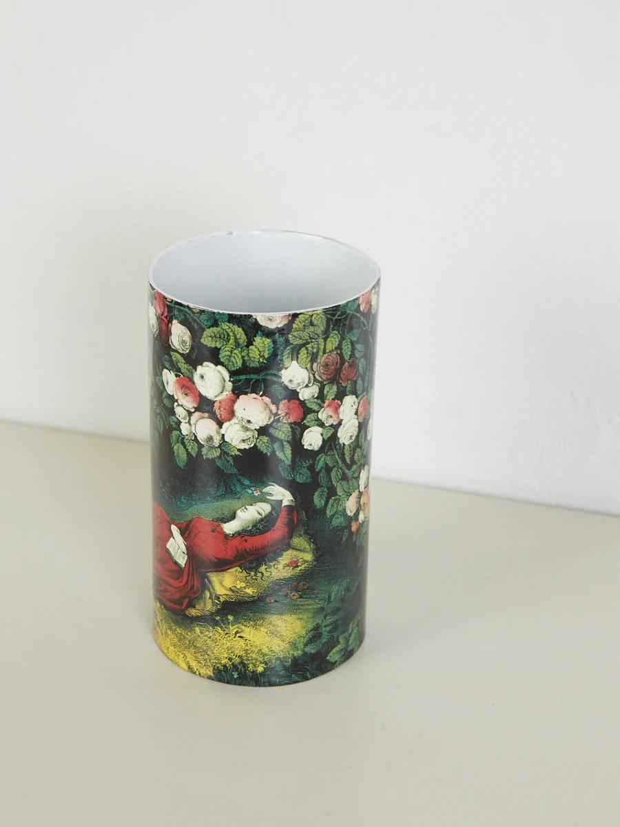 Cylindrical vase with painting of person under rose arch. White interior. Light surface, plain wall background.