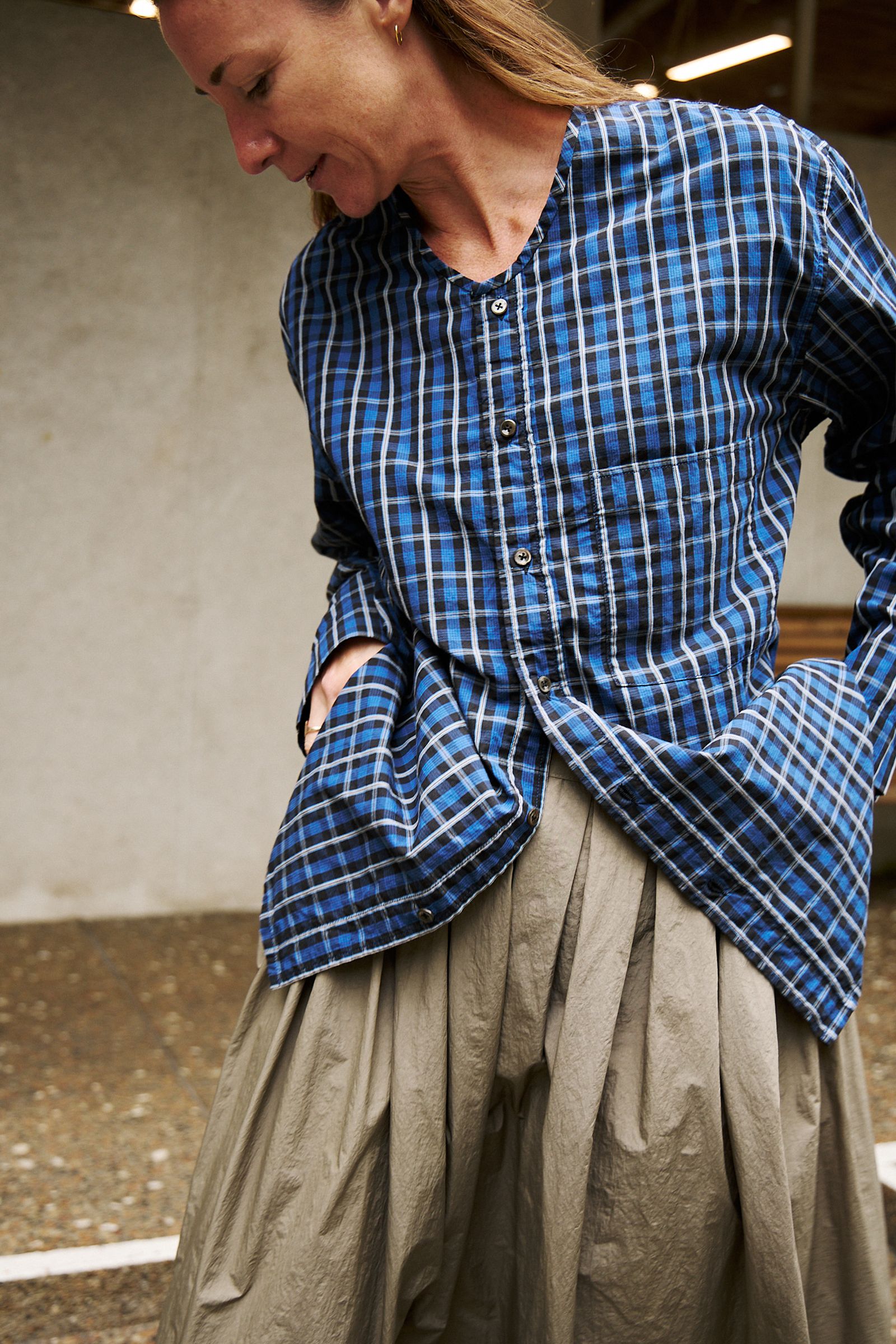 close up of check shirt worn open over skirt with hands in pocket