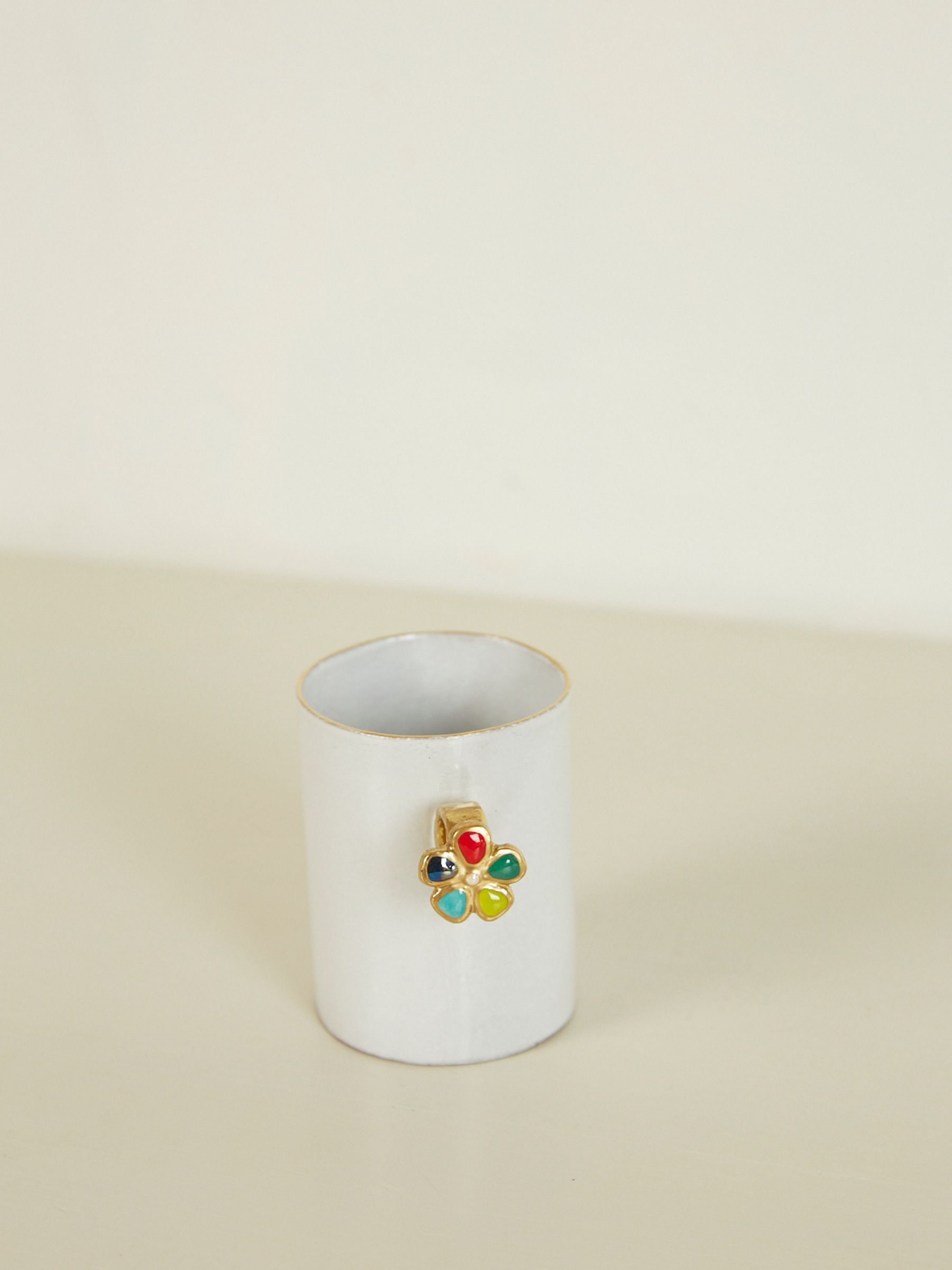 White ceramic mug with small floral-shaped handle. Colourful centre on handle. White surface and background.