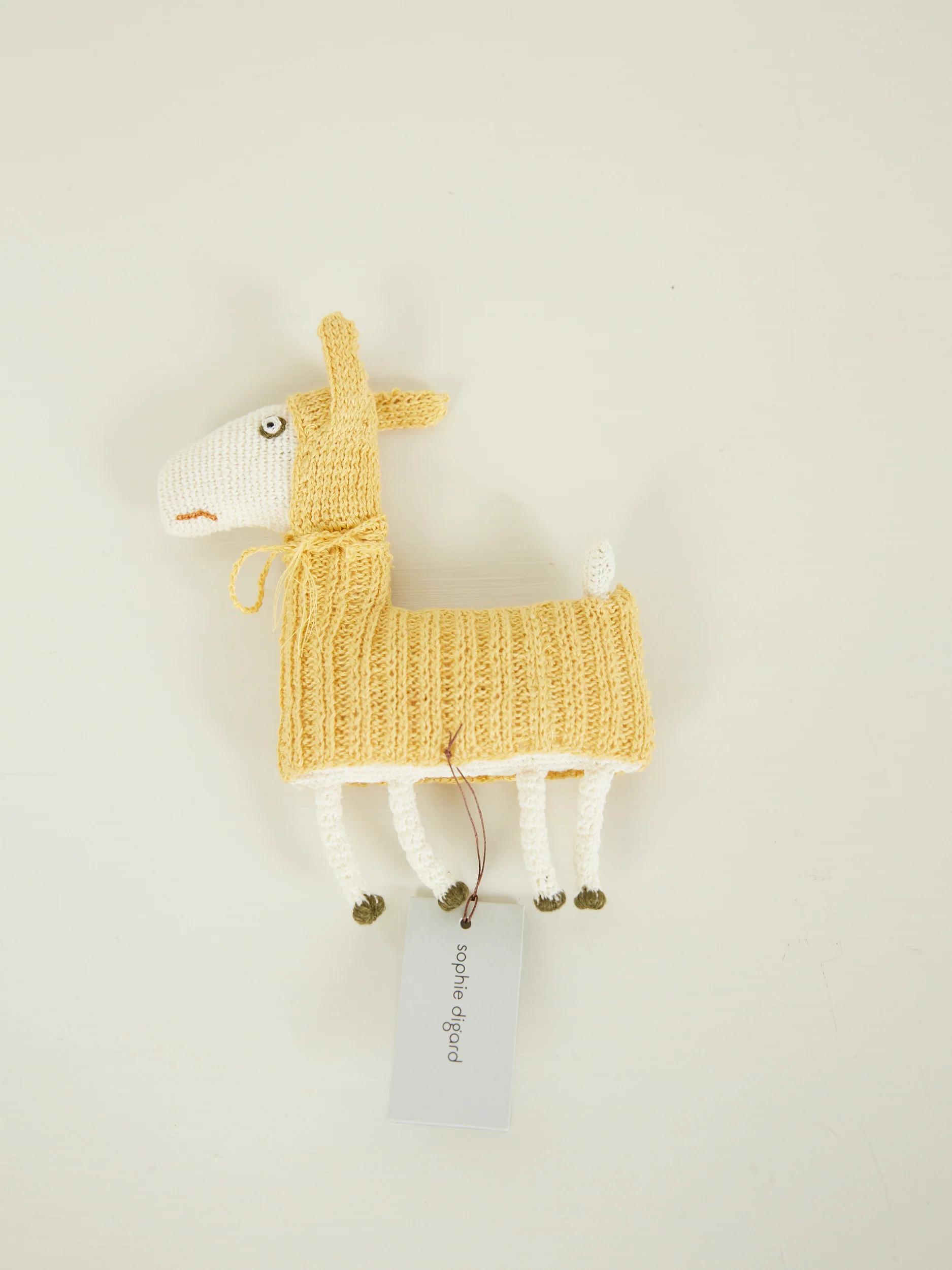 Knitted toy llama in yellow sweater. White body, beige face. Tag on leg.