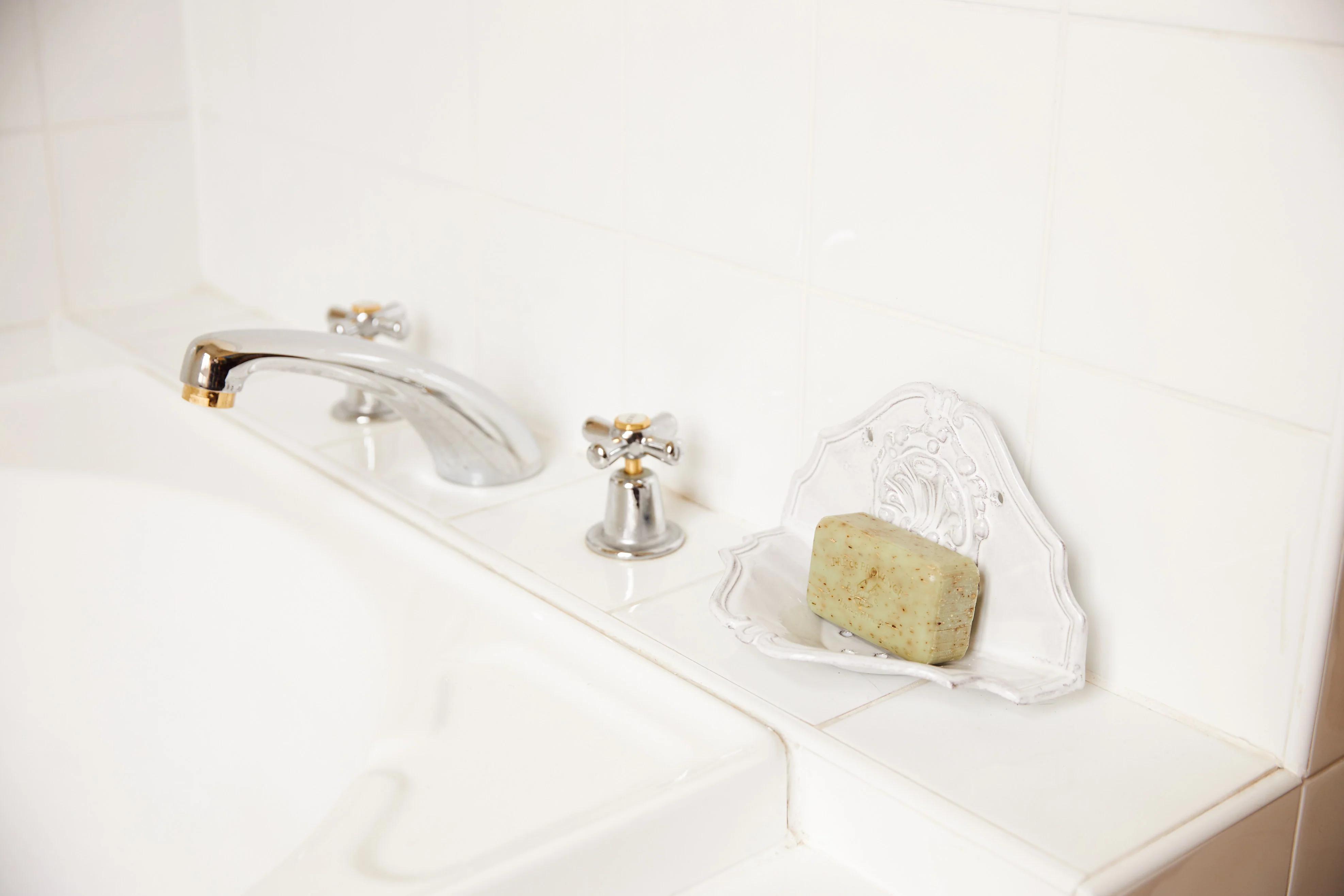 Bathroom sink with silver faucet. Decorative soap dish with textured soap. White tiled wall background.