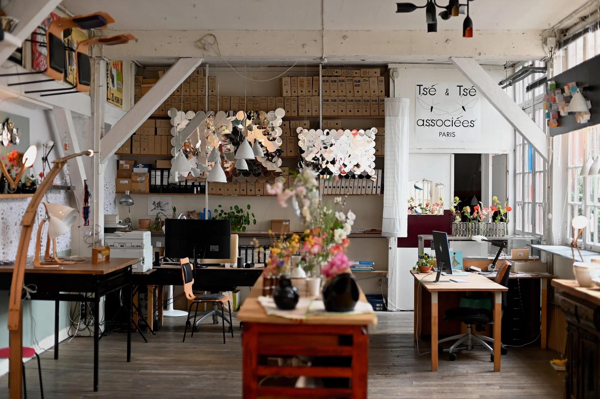 Bright eclectic office with decor, plants, and shelves. Paper decorations on wall. Sign reads "Tsé & Tsé associées Paris".