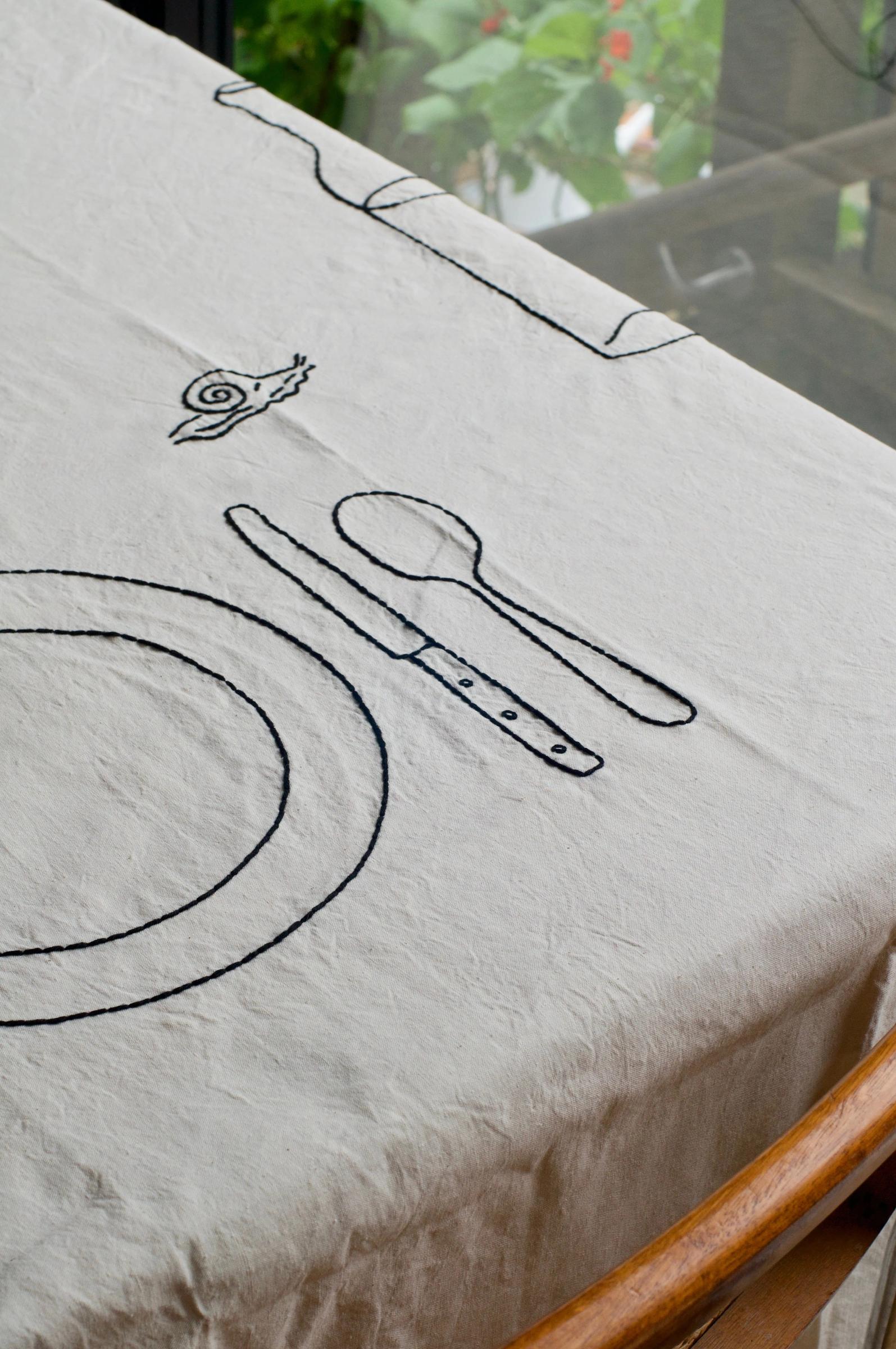 White tablecloth with black outlines of plate, utensils, and snail. Partial border visible at top.
