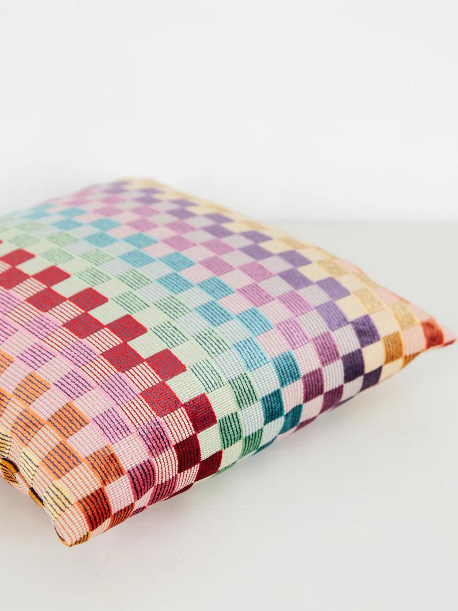 Colourful checkered cushion with pastel and vibrant hues. White background, light-colored surface.