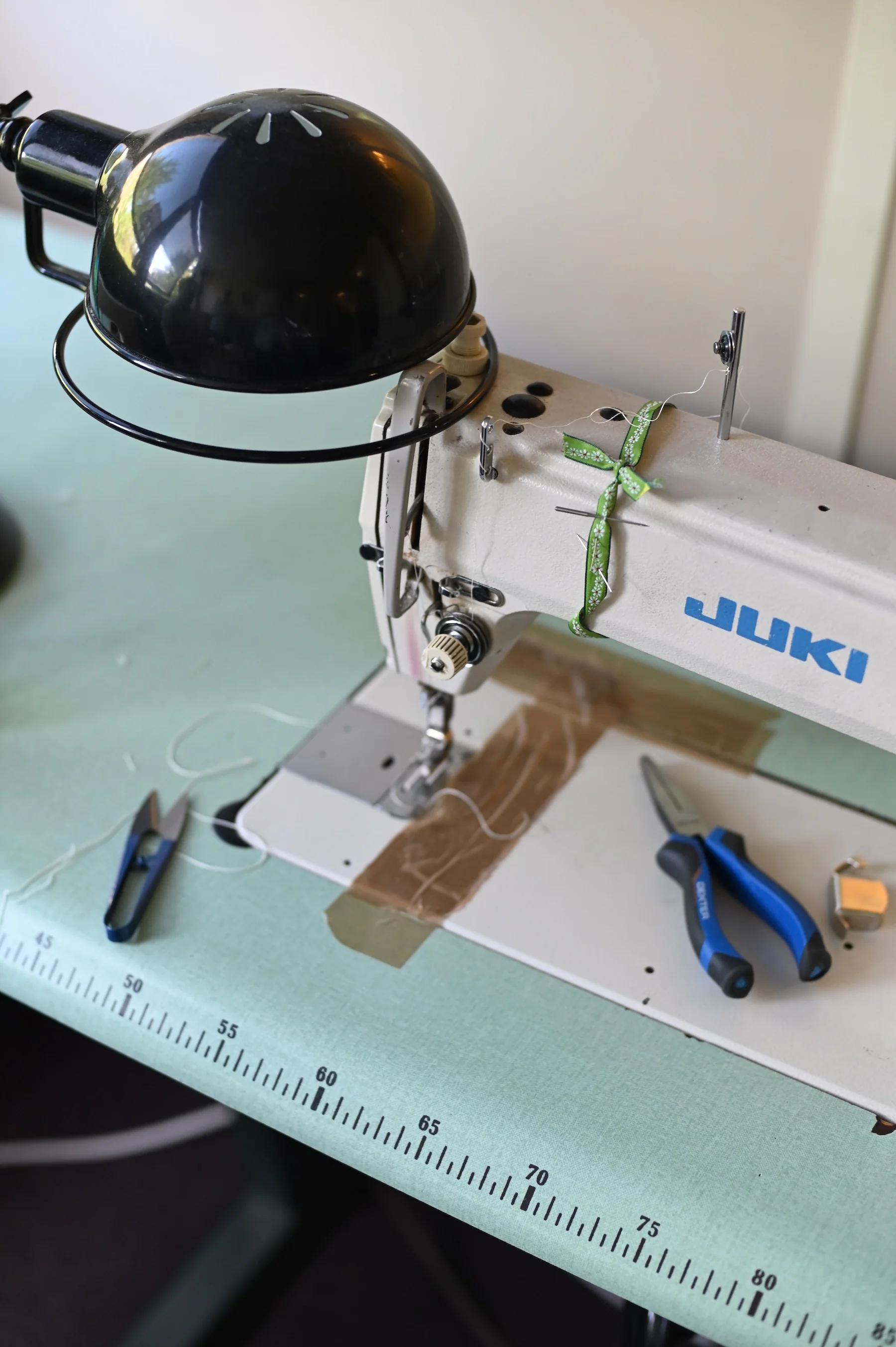 Sewing machine on green table with ruler edge. Scissors, thread, and box nearby.