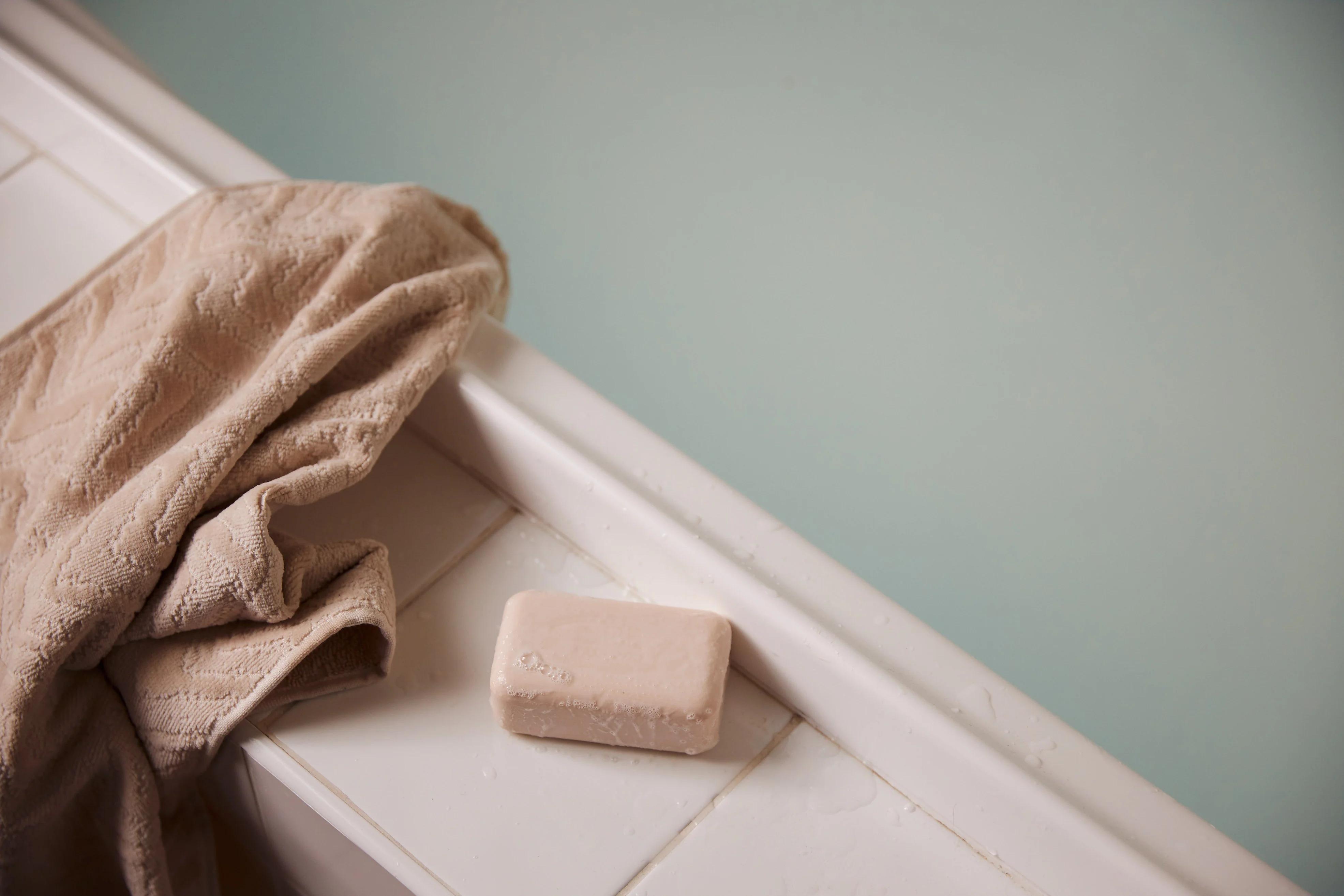 Beige towel over bathtub edge with soap bar. Water-filled tub creates calm, clean atmosphere.