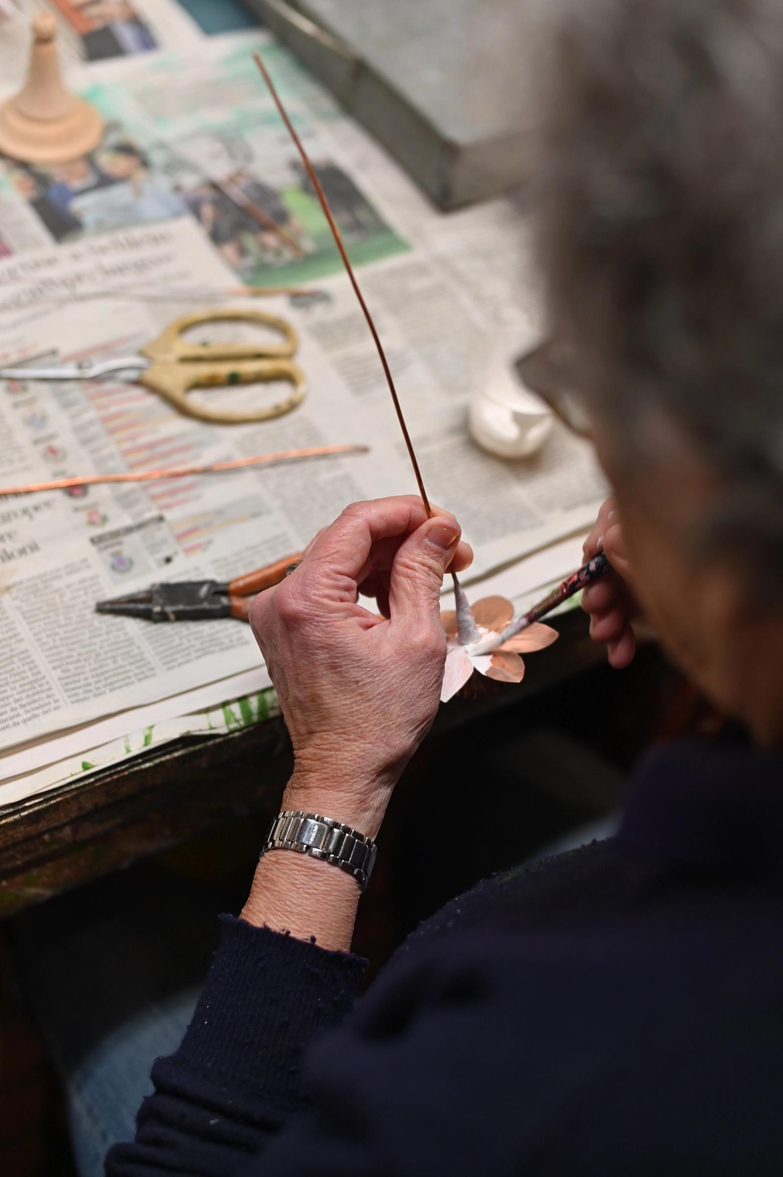 Betty painting a copper flower at her workbench