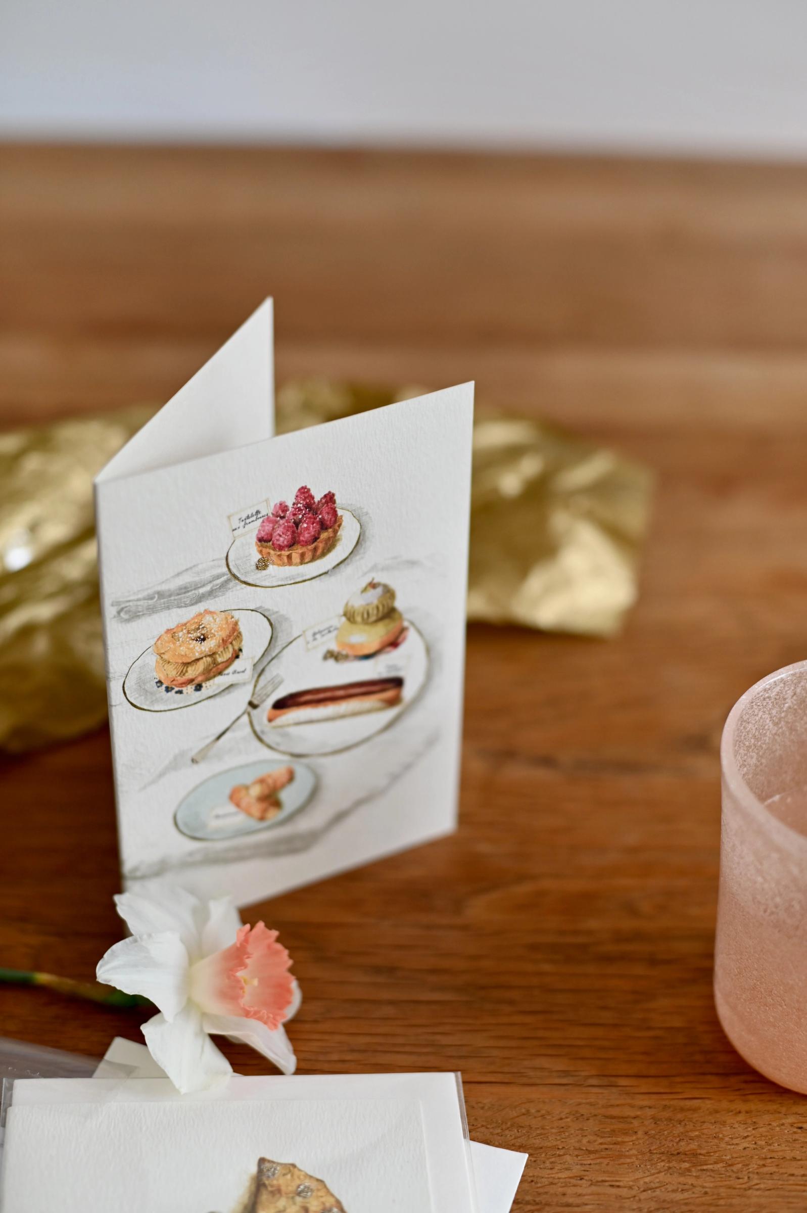 A greeting card with an illustration of french patisserie in soft tones. The card is upright against a white background.