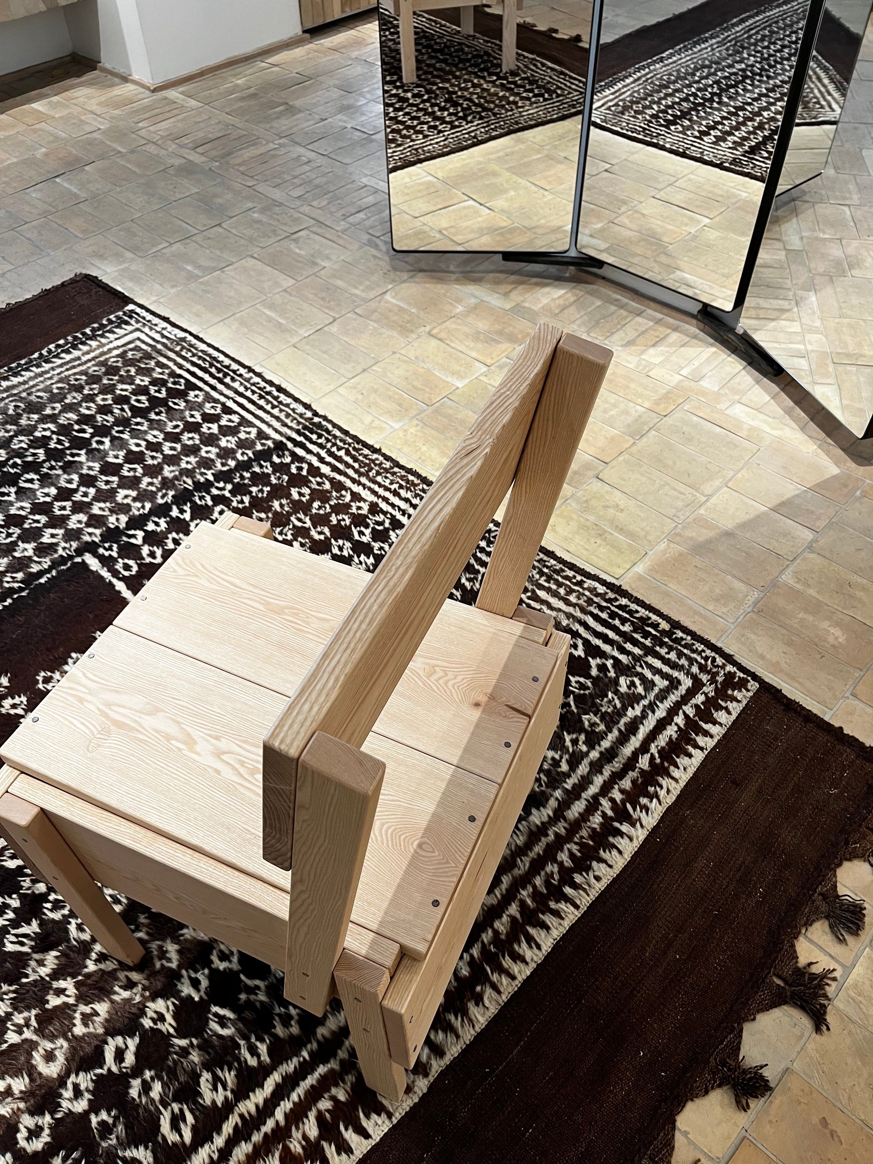 Wooden chair on decorative rug near three-paneled mirror. Light-colored tiled floor.