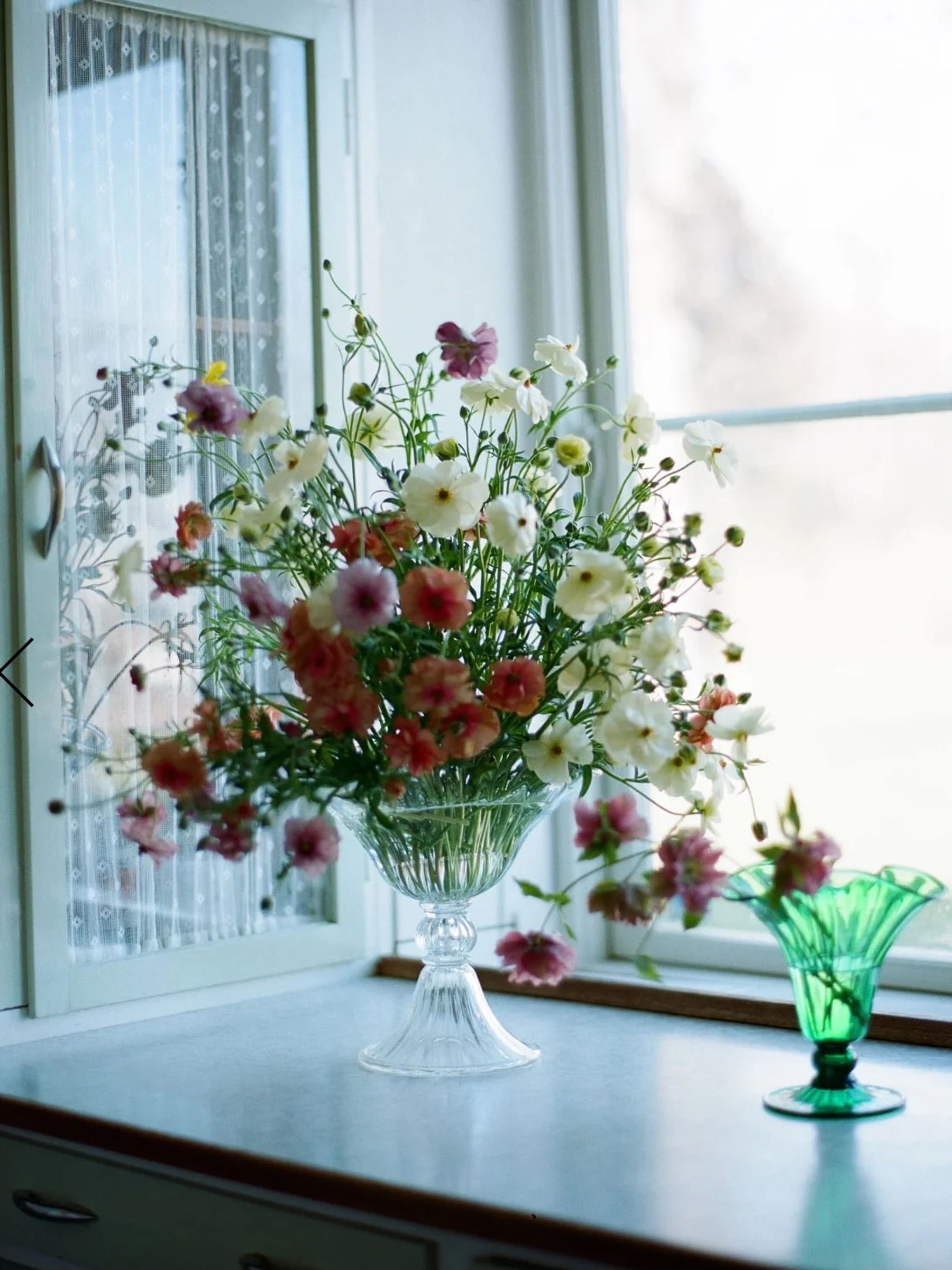 large clear vase holds fresh flowers next to open windowsill in bright light