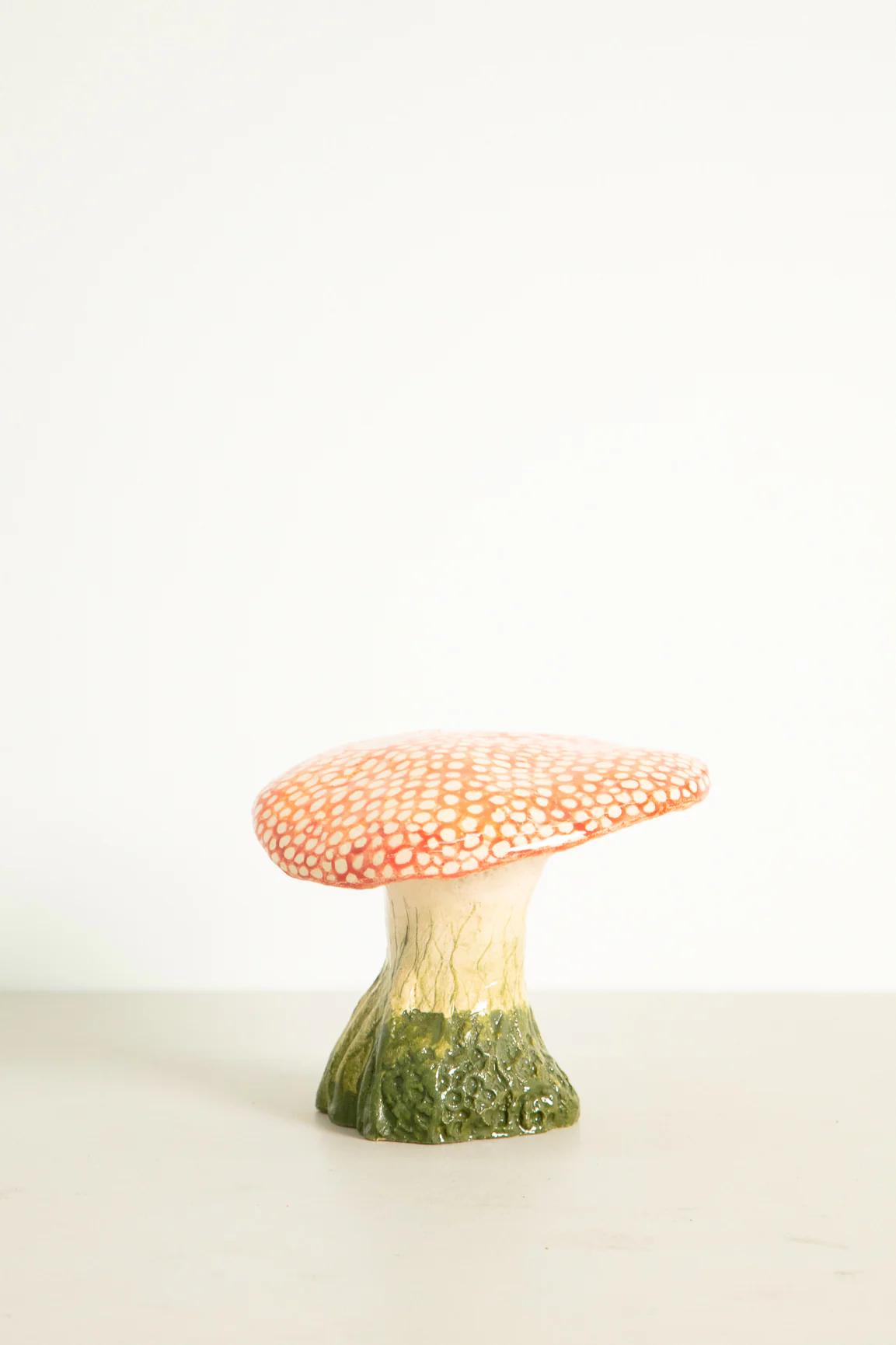 Ceramic mushroom sculpture with textured red-orange cap and white dots. Stem transitions from white to green at base.