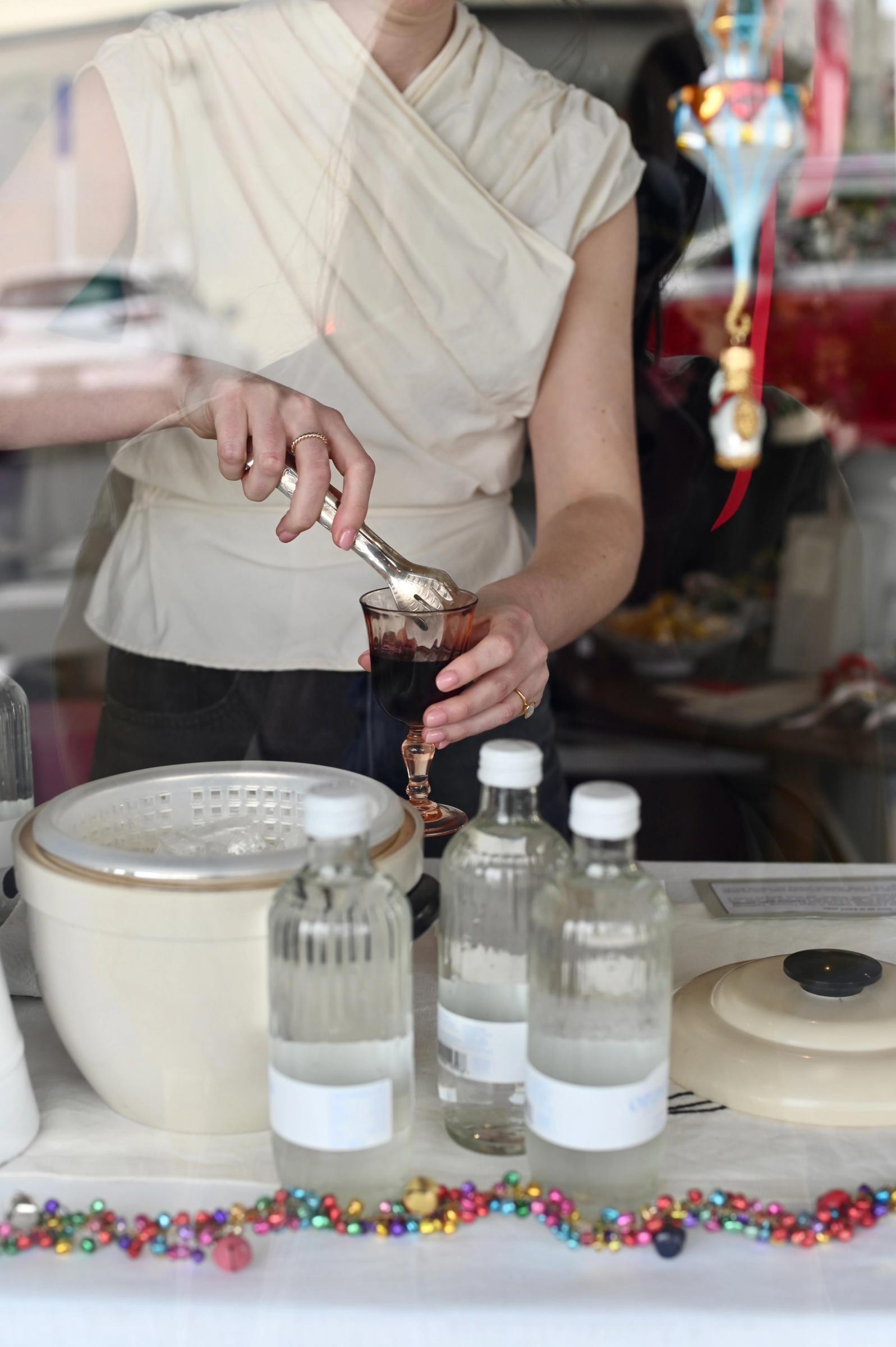 woman adding ice to glass with silver cocktail tongs