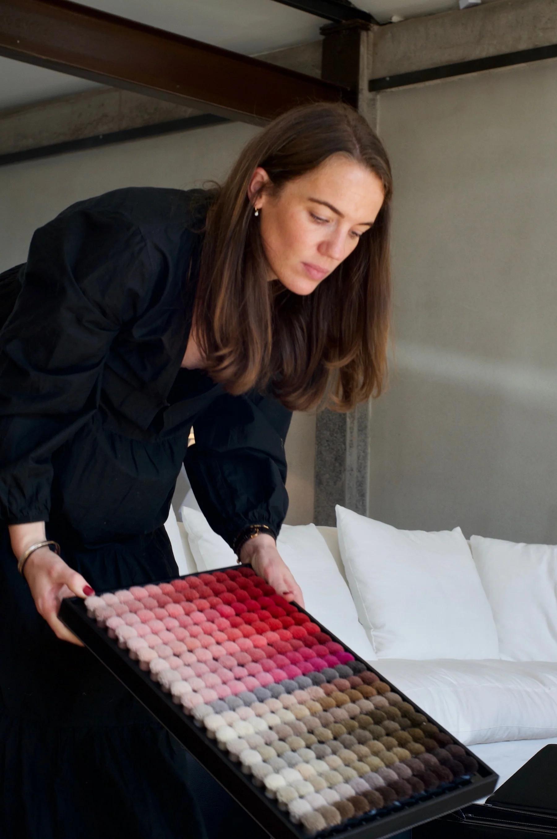 Woman in black examining fabric swatches. Minimalist room with white sofas in background.