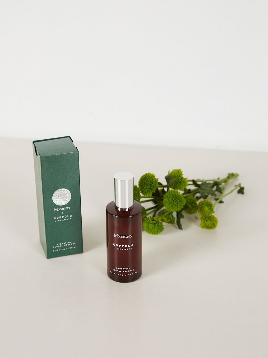 a green box and brown glass bottle sit on table next to green blooms