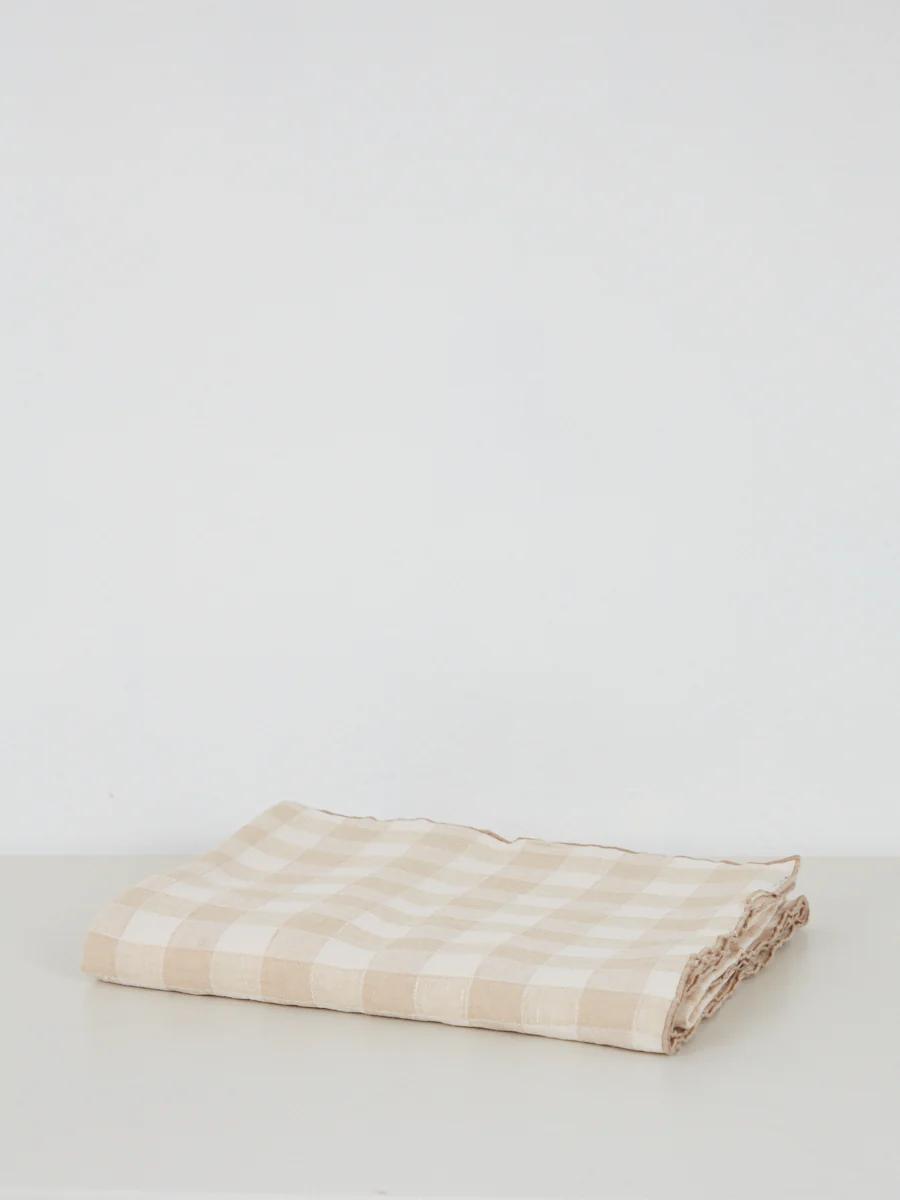 Folded beige and white checkered cloth on light surface. White background. Soft material with simple design.