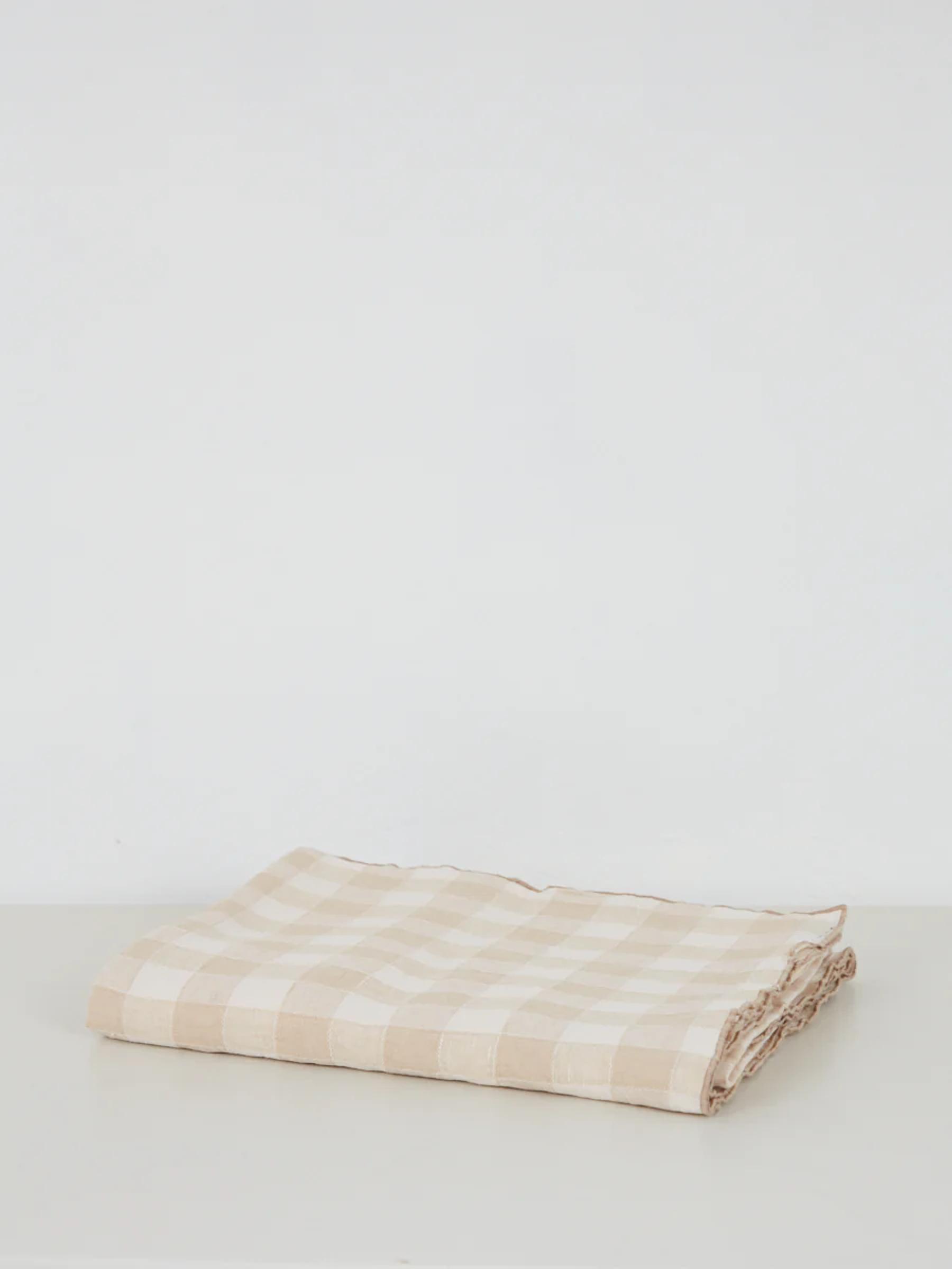 Beige and white checkered cloth neatly folded on light surface. Neutral background.