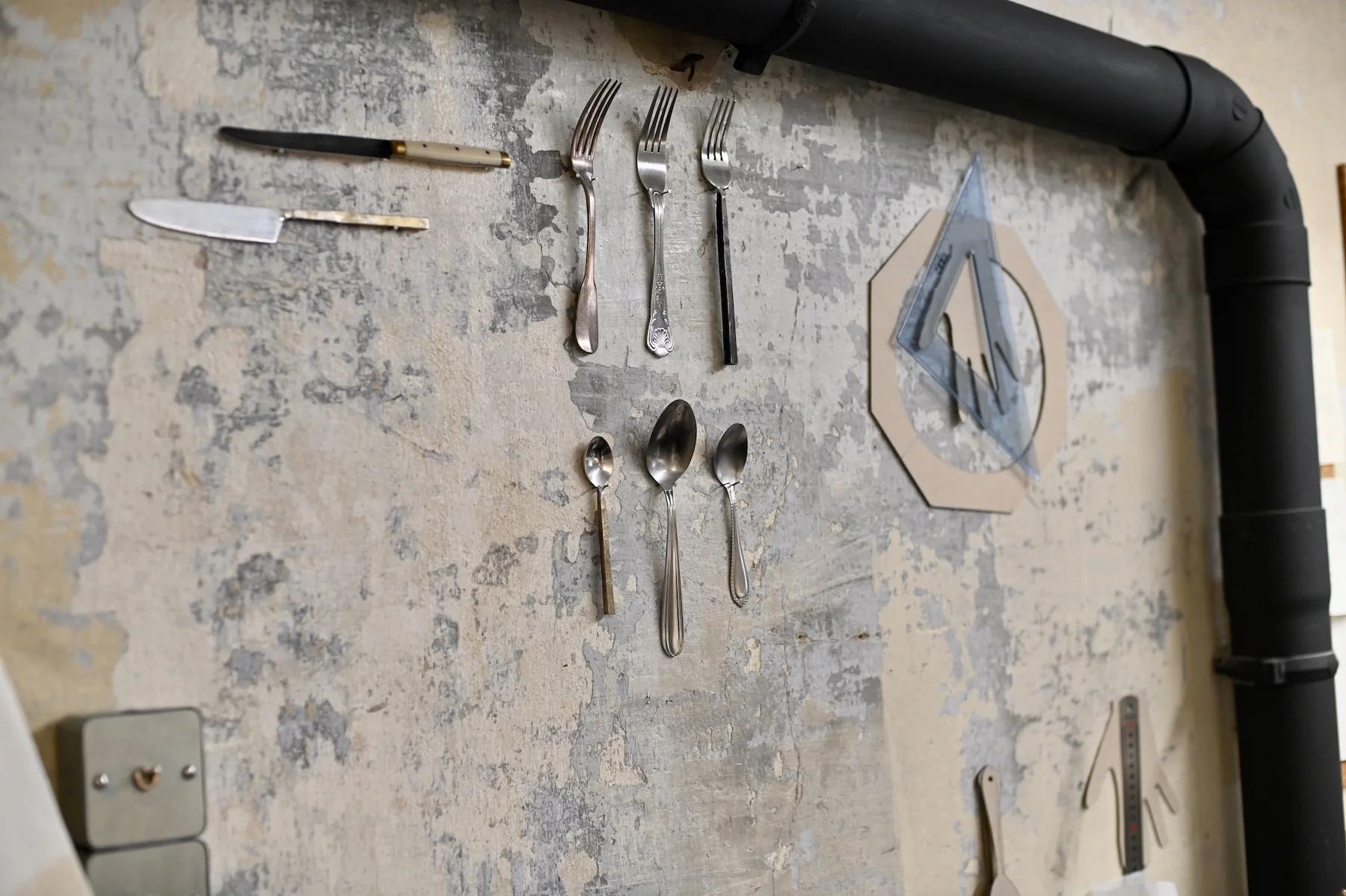 Silverware arranged artistically on textured wall beside black piping.