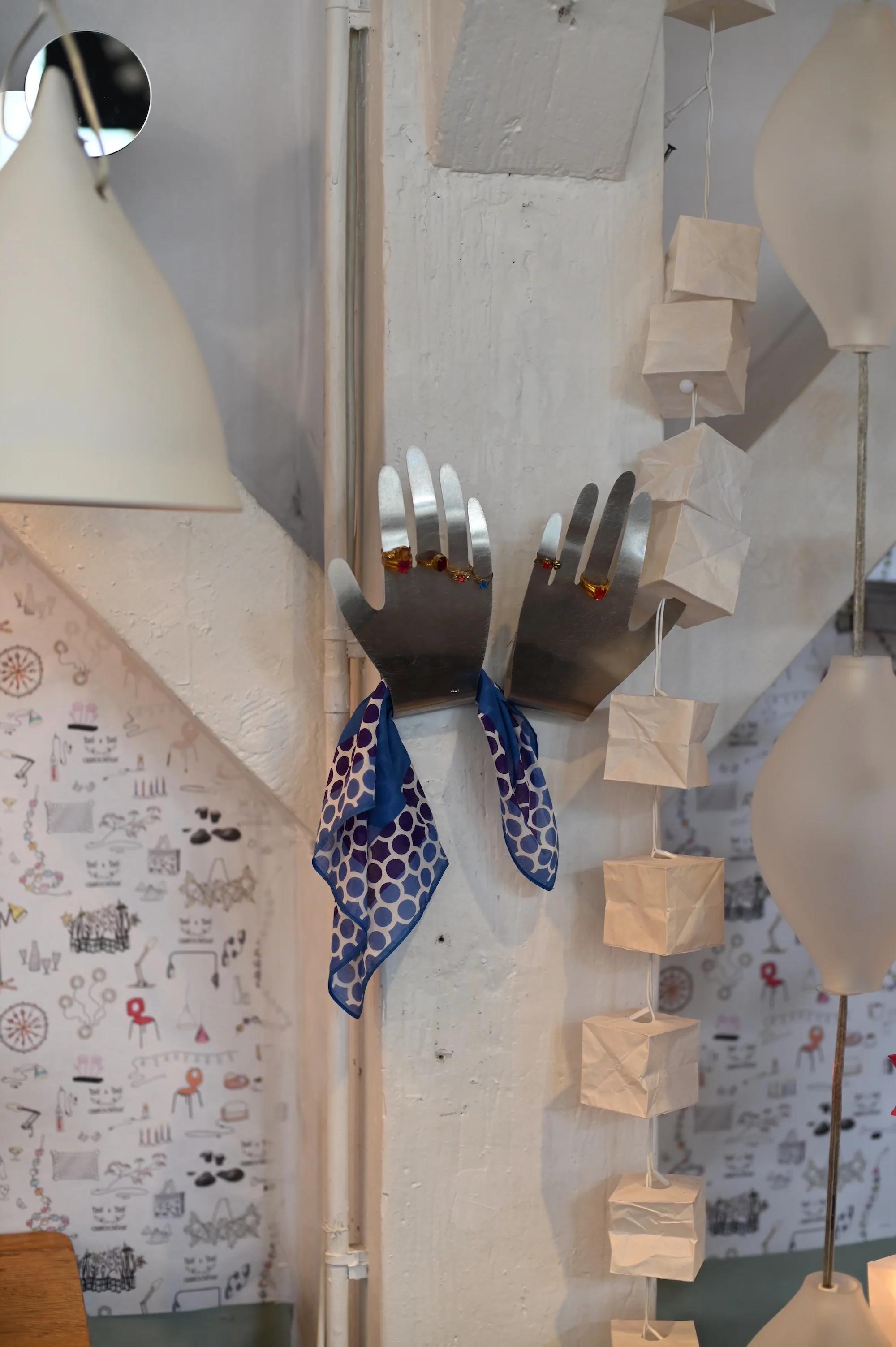 Wall with metallic hand-shaped hooks holding blue polka dot scarf. Cat-patterned wall, paper lanterns, white lamp visible.