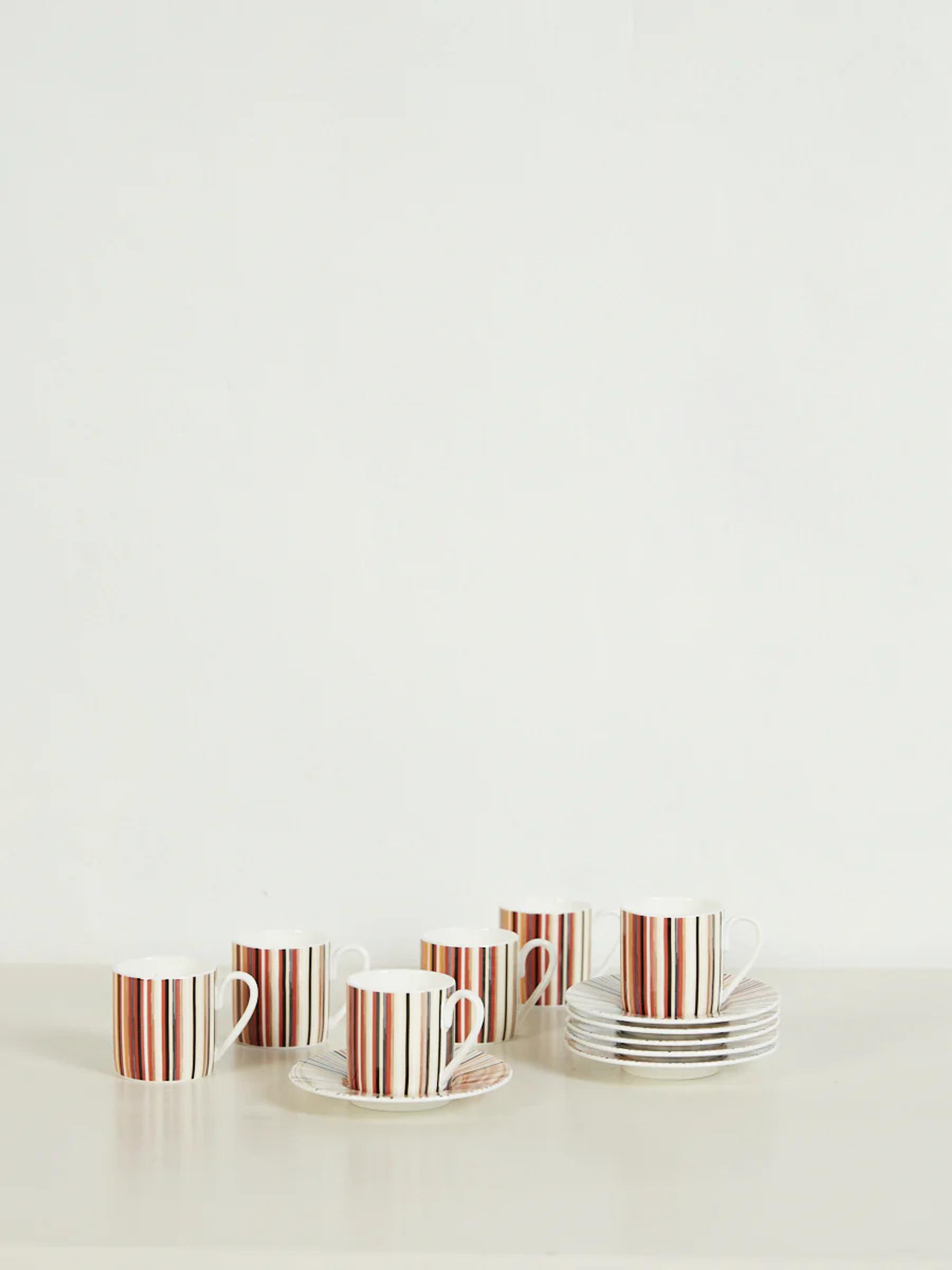 Stacked teacups and saucers with brown and orange vertical stripes on white surface. Plain background.