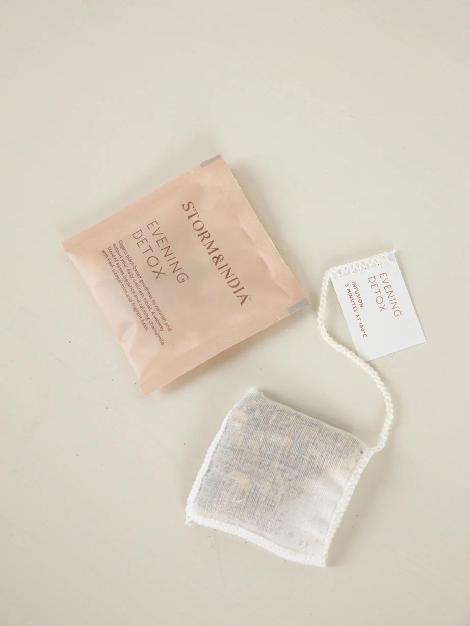 Beige "Storm + India Evening Detox" tea packet and individual teabag on light surface. White tag on teabag matches packet label.