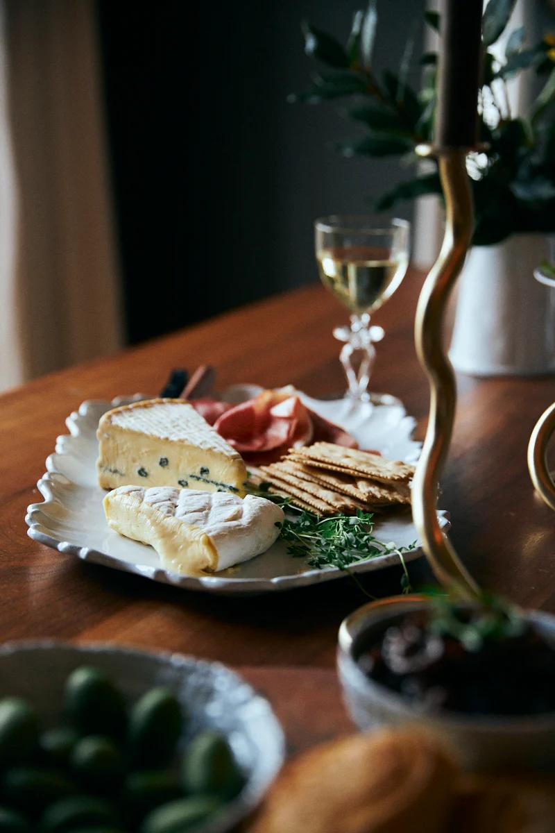 Cheese, meat, and crackers platter with wine. Olives, nuts, and mostarda nearby. Partial view of candleholder.