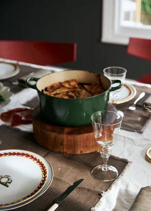 Colourful plate with green beans, roasted potatoes, and beef casserole. Black bottle, green pot, glassware on grey tablecloth.