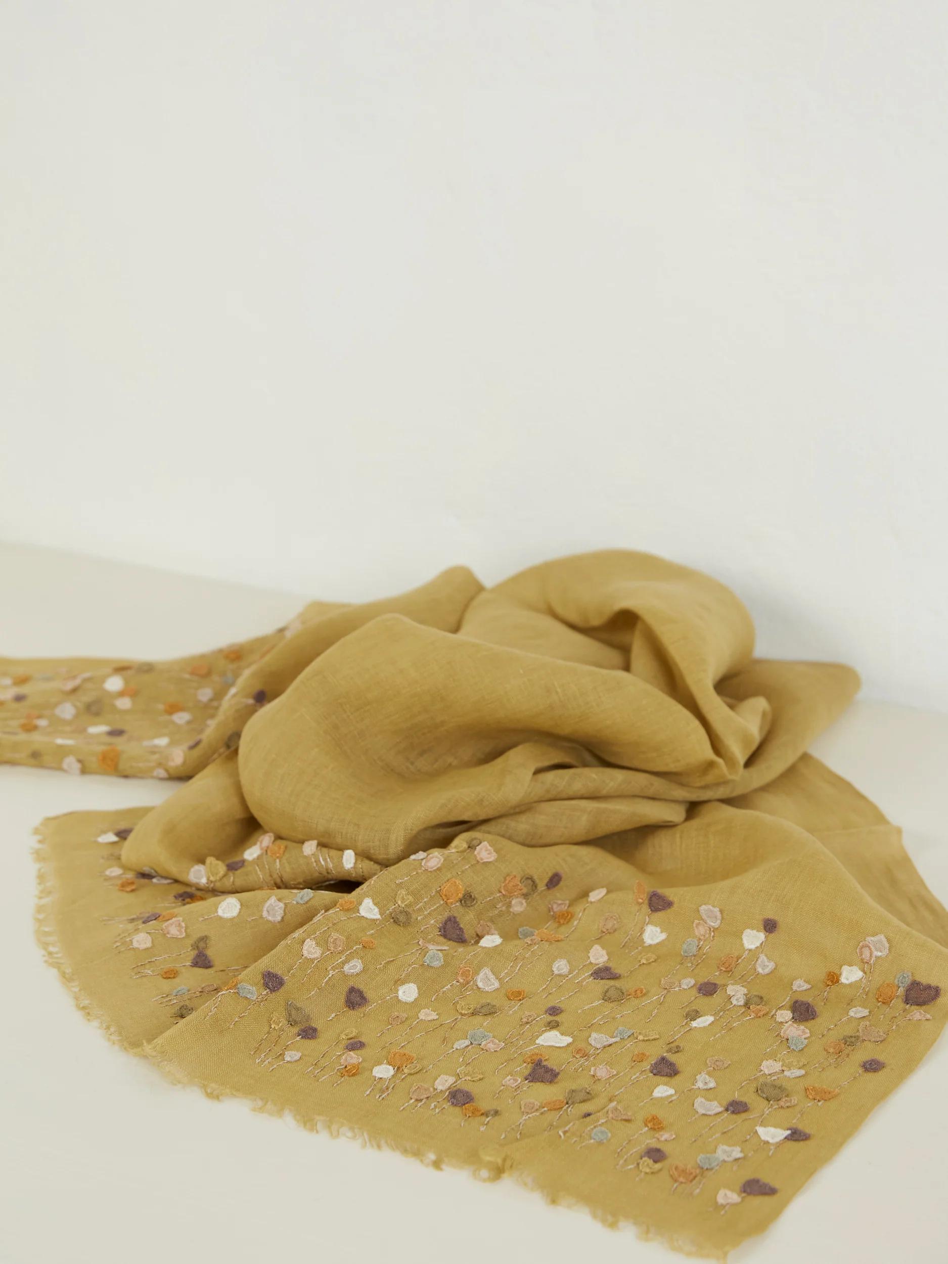 Mustard-coloured scarf with scattered floral embroidery. Lightweight, textured fabric with frayed edges.