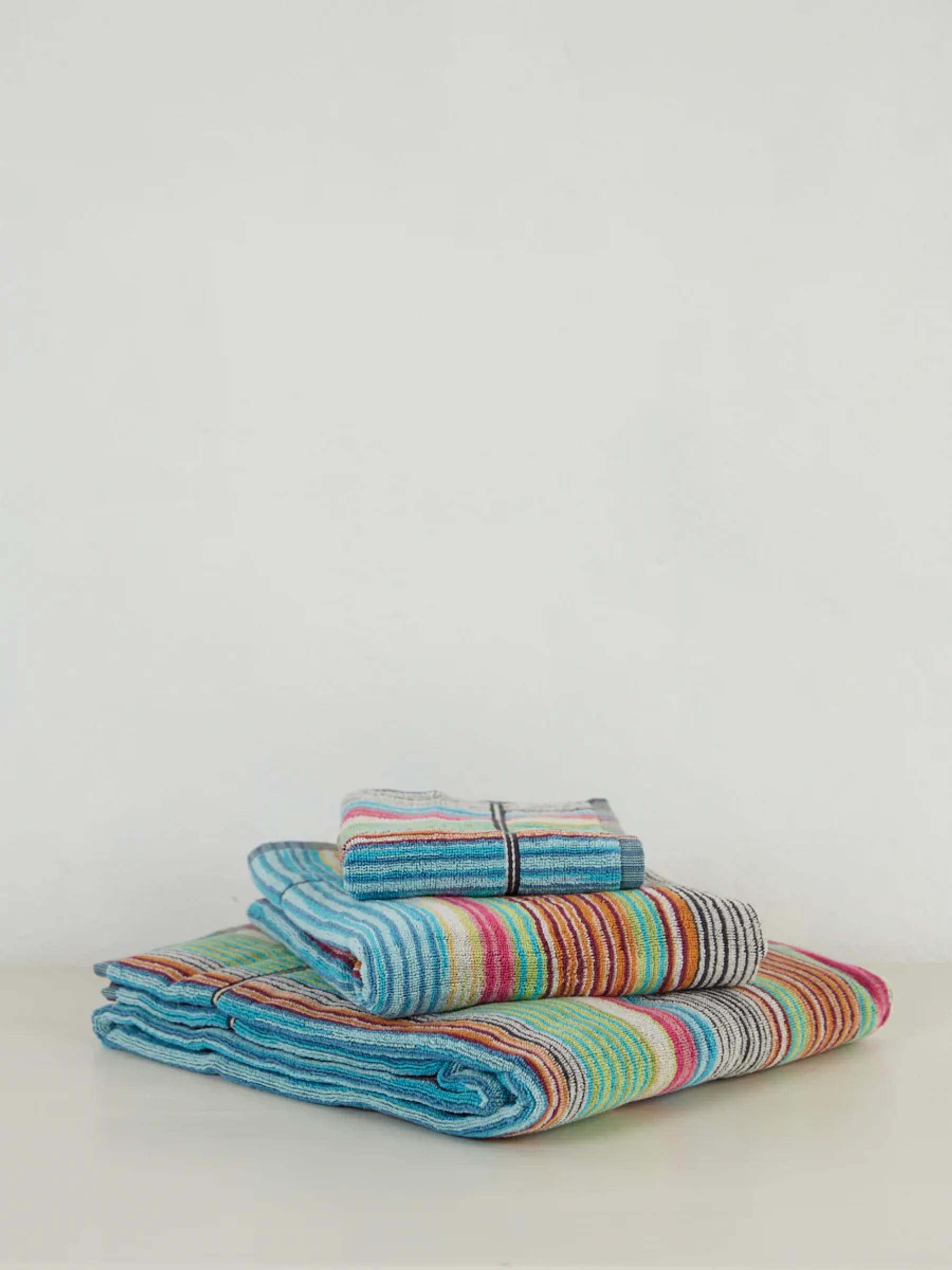 Folded multicoloured striped towels by Missoni. The stack includes various sizes, featuring vibrant stripes in blues, reds, greens, and other hues.