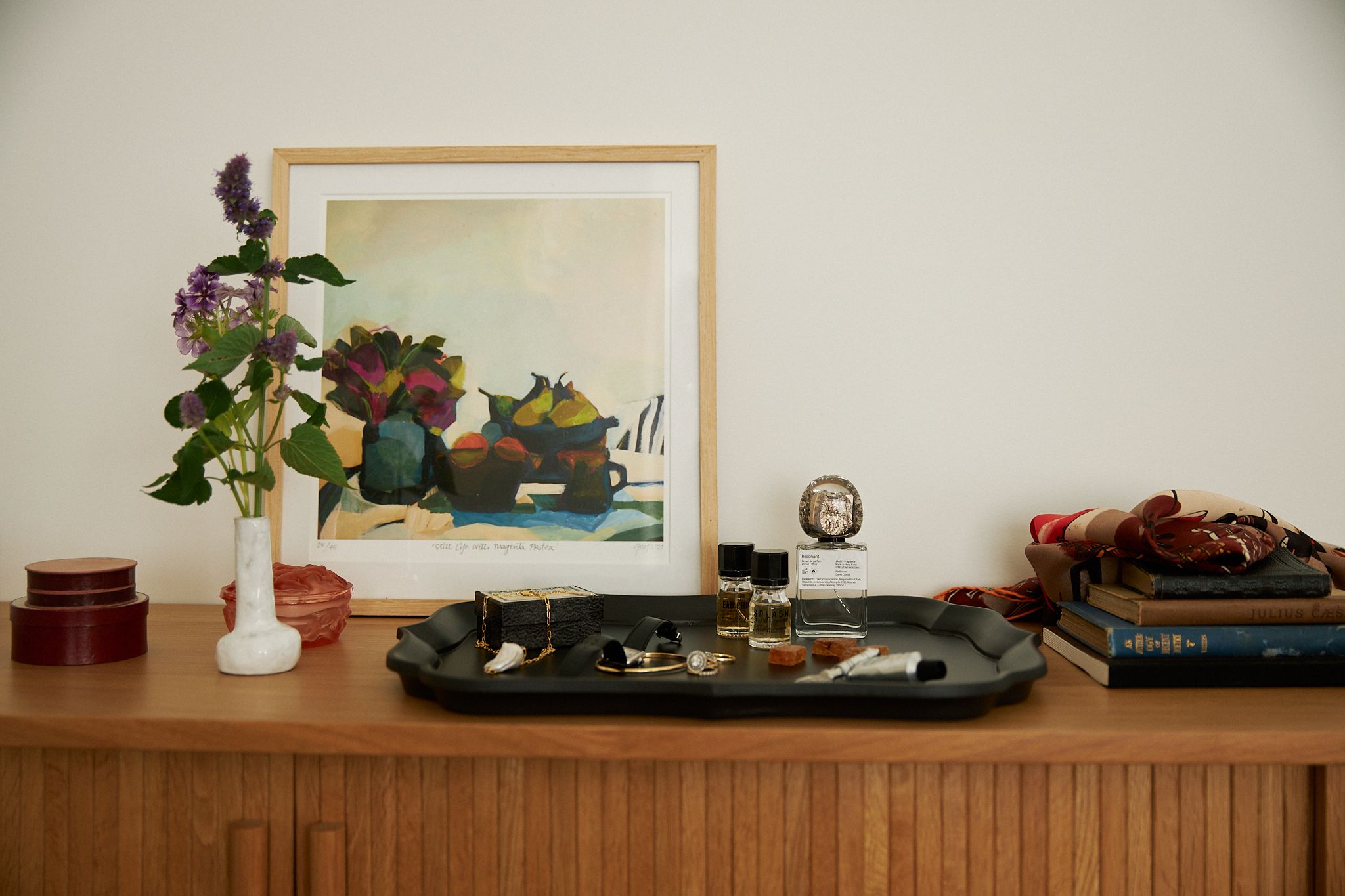 a landscape image of the top of a dresser adorned in objects such as flowers trays and books