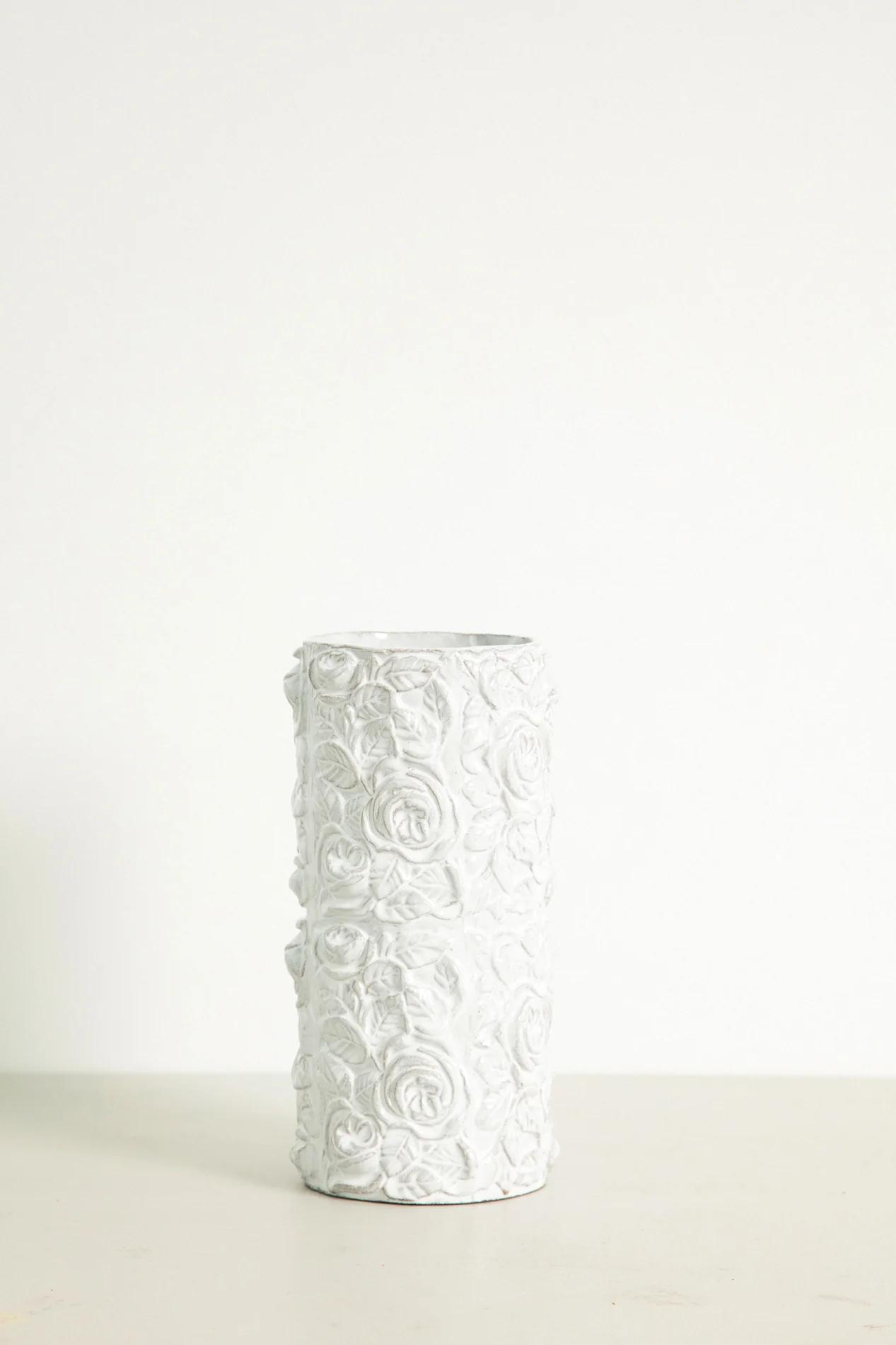 Tall white ceramic vase with raised floral pattern covering entire surface. Light-coloured background.