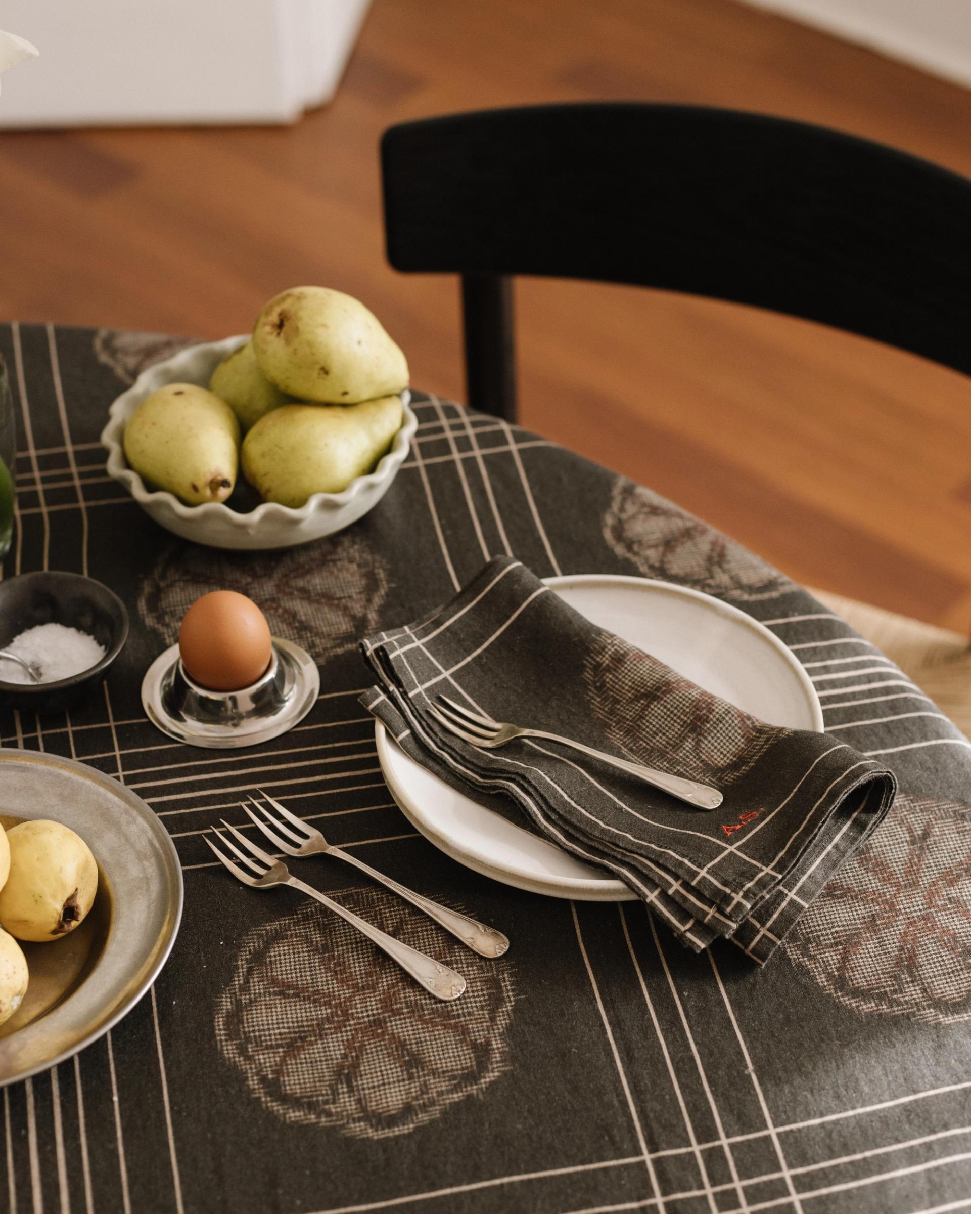 crop of a round table in dark grey tablecloth with brown details and a bowl of pears