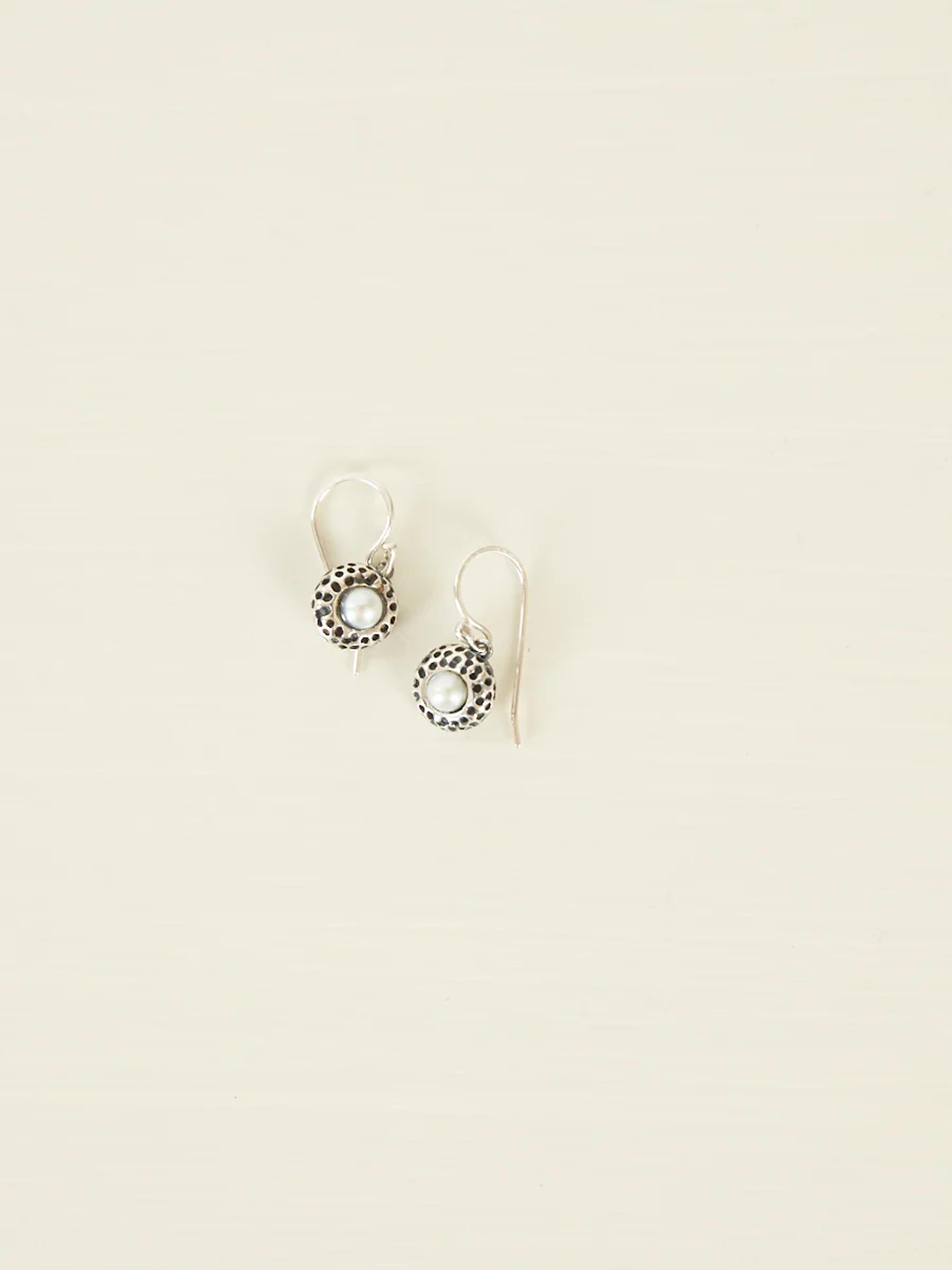 Silver earrings with circular designs and central white bead. Simple hook for wearing. Light background.