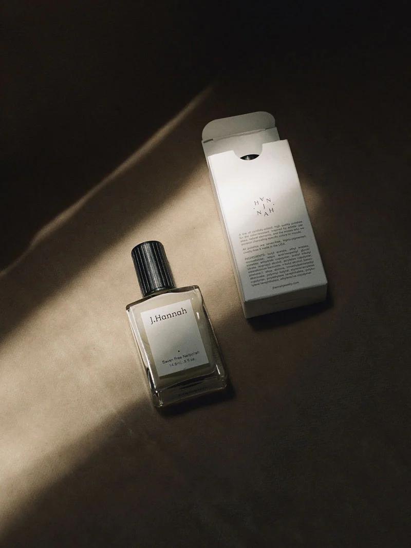 A bottle of J. Hannah perfume rests next to its white packaging on a dark surface, with light casting a soft shadow across the scene. The image highlights J. Hannah’s attention to detail.