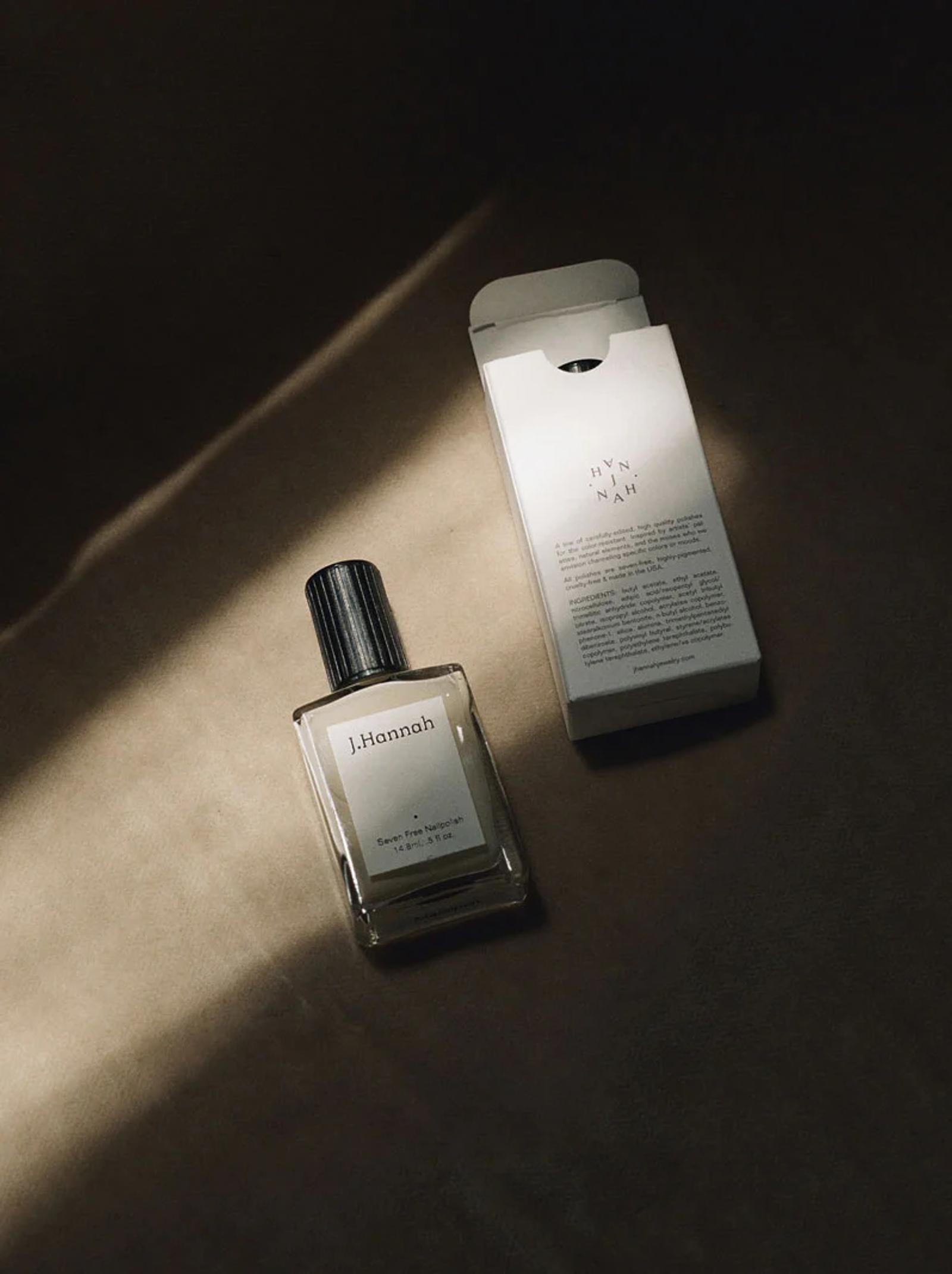 A bottle of J. Hannah perfume rests next to its white packaging on a dark surface, with light casting a soft shadow across the scene. The image highlights J. Hannah’s attention to detail.