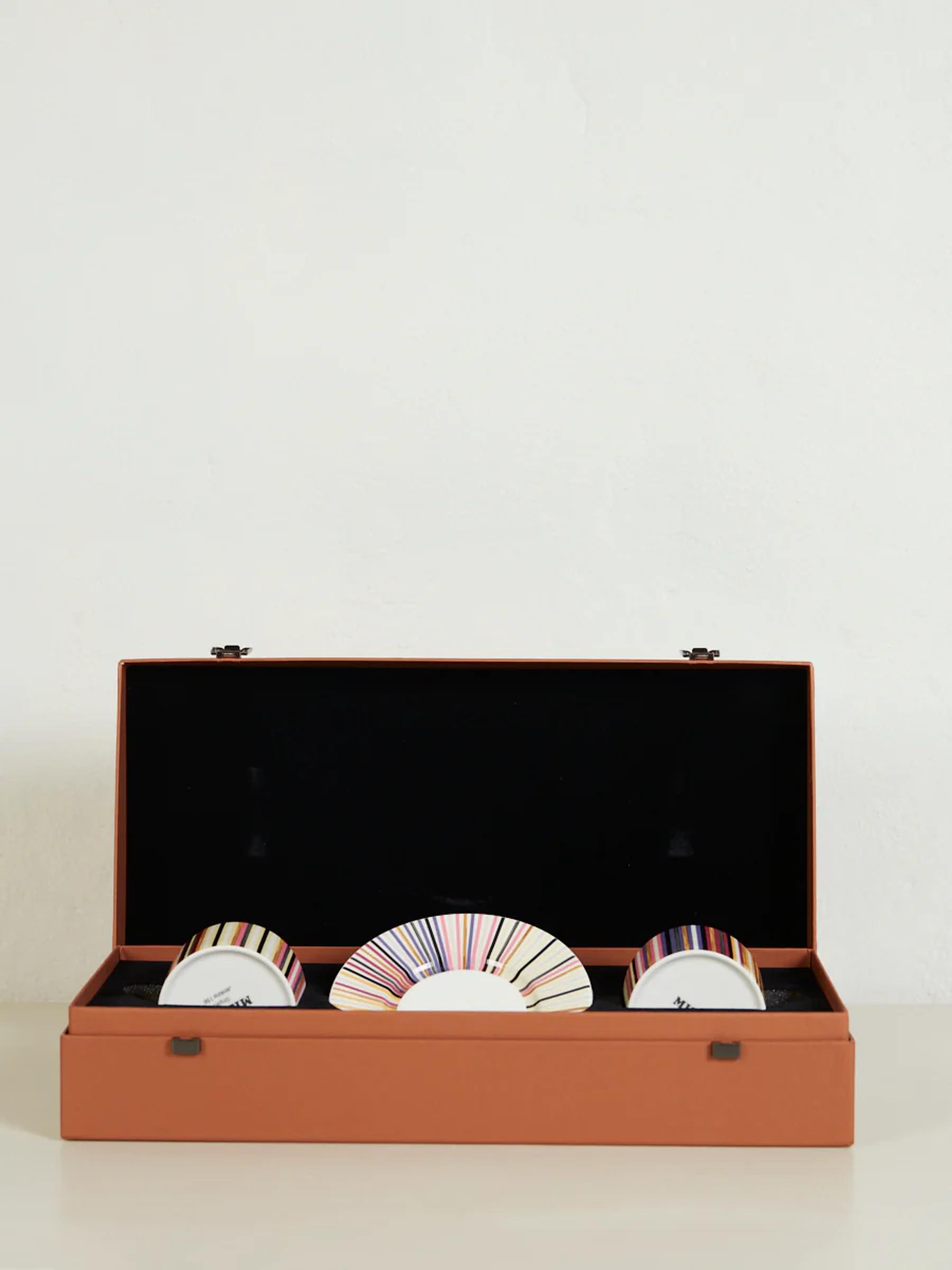 Brown box with black interior holds cylindrical objects with multicoloured striped designs. White background.