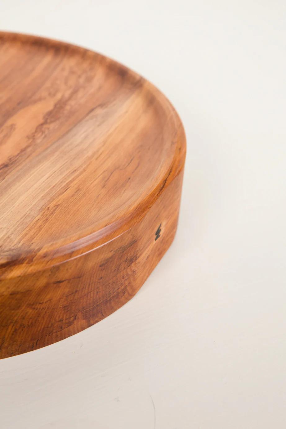 Close-up of round wooden cutting board edge, showing smooth surface and natural grain. Handcrafted using traditional turning techniques, highlighting NZ wood beauty against off-white background.