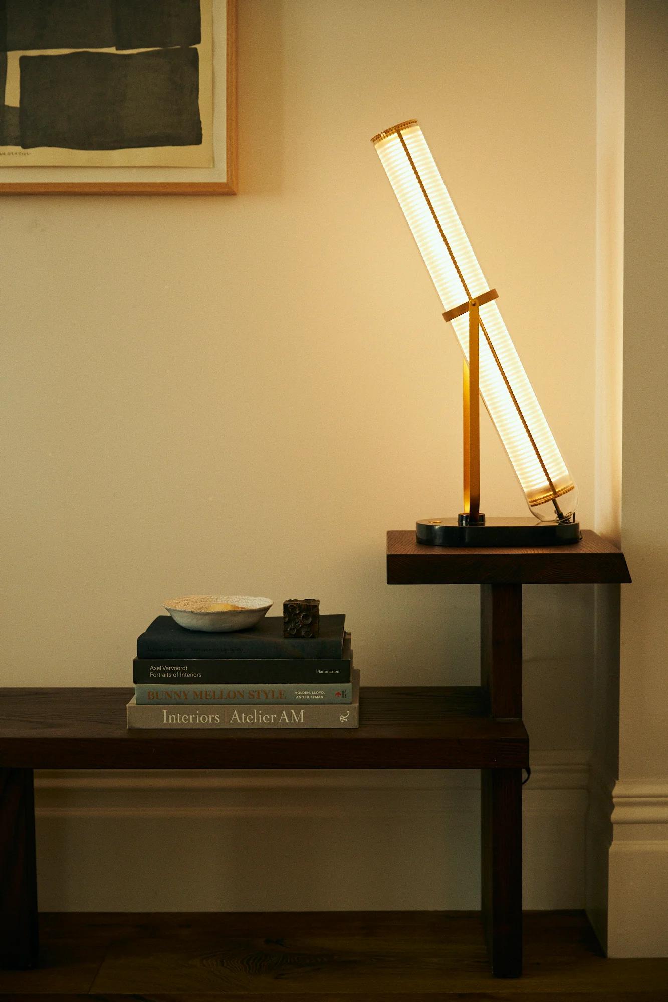 Table lamp on wooden side table. Books, small dish, and decorative object below. Abstract art on wall.