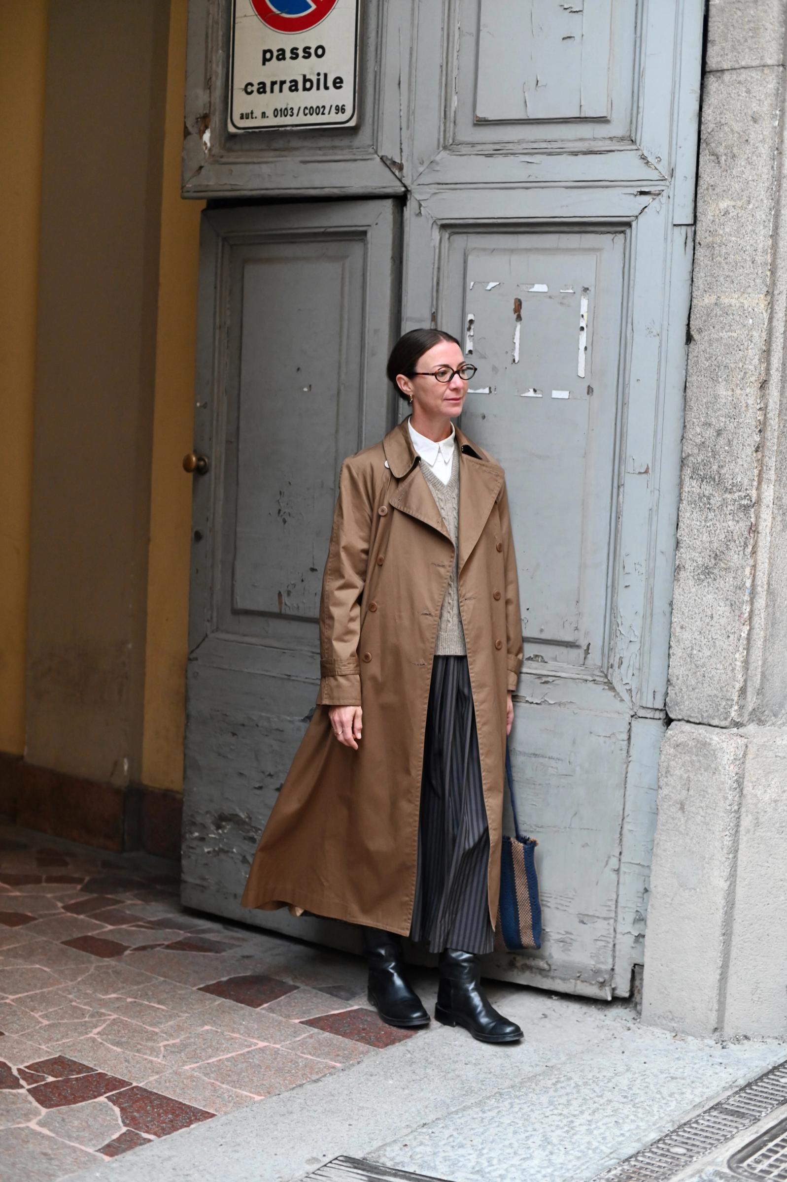 woman standing in front of blue door wearing a bronze trenchcoat