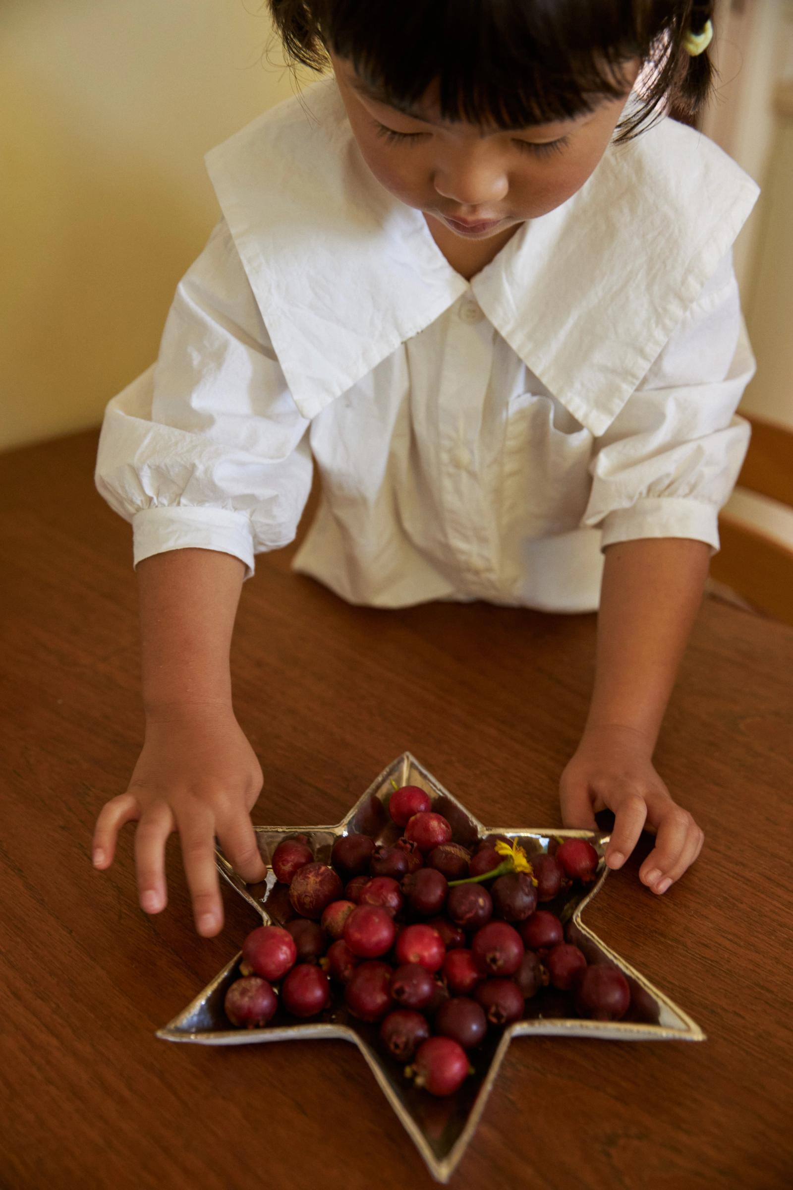 small girl places fresh guavas in a silver star plate