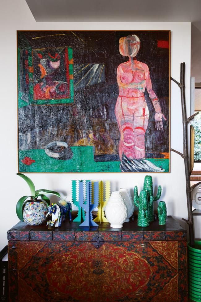 Decorated chest with colourful sculptures, vases, and glass orb. Large abstract painting above. Industrial lamp to the right.