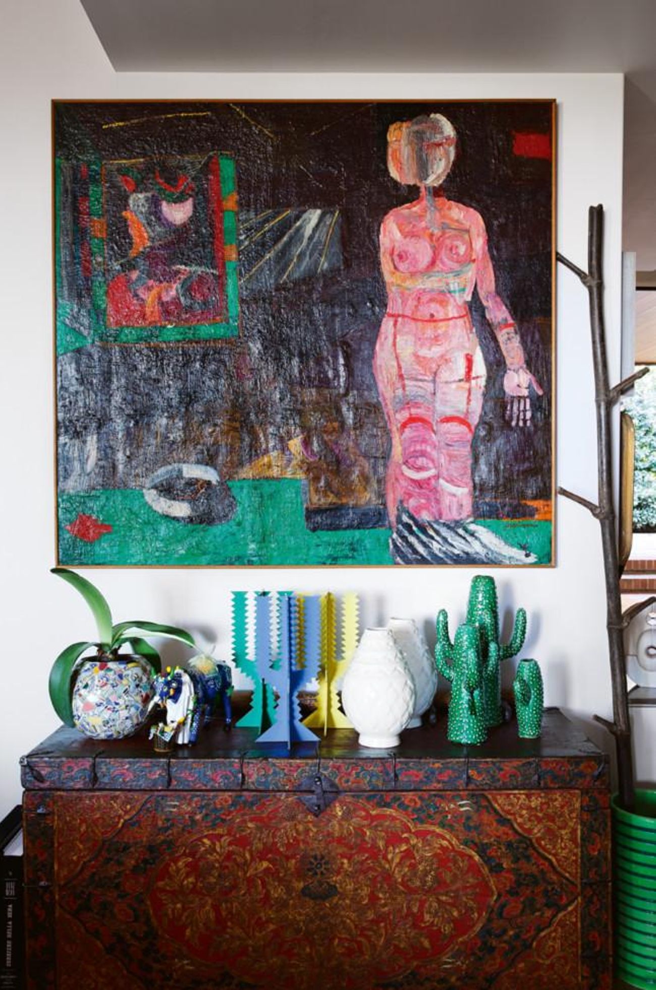 Decorated chest with colourful sculptures, vases, and glass orb. Large abstract painting above. Industrial lamp to the right.