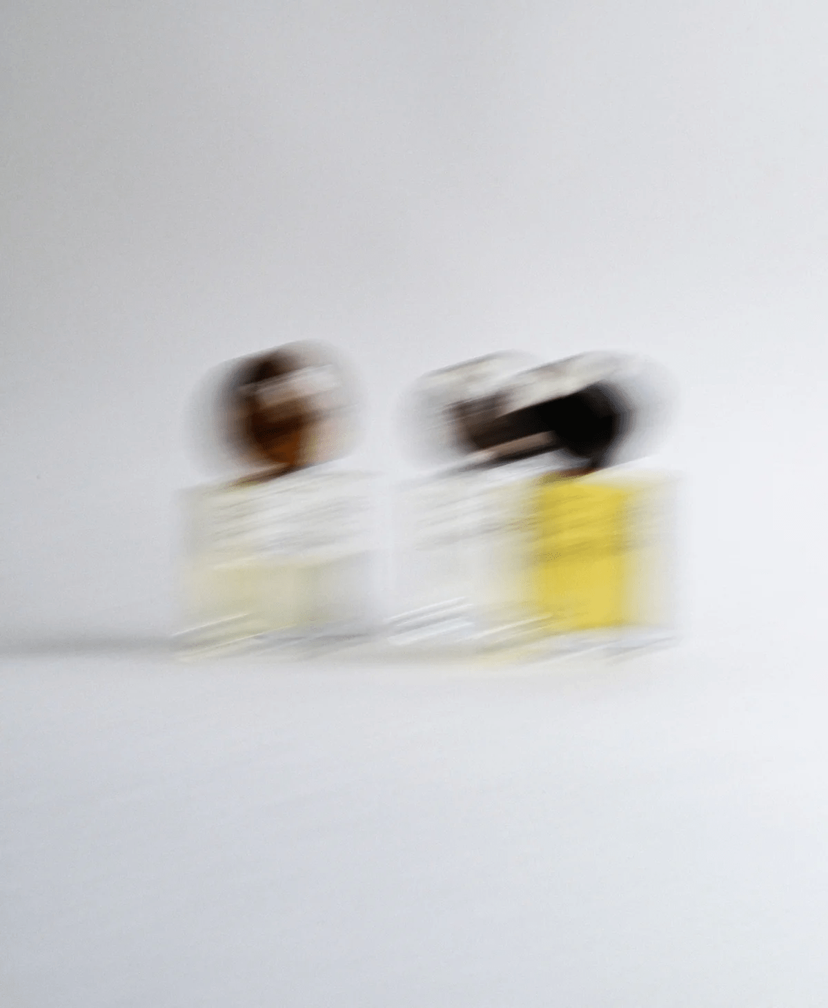 Blurry image of two glass bottles with yellow and brown liquid against grey background.