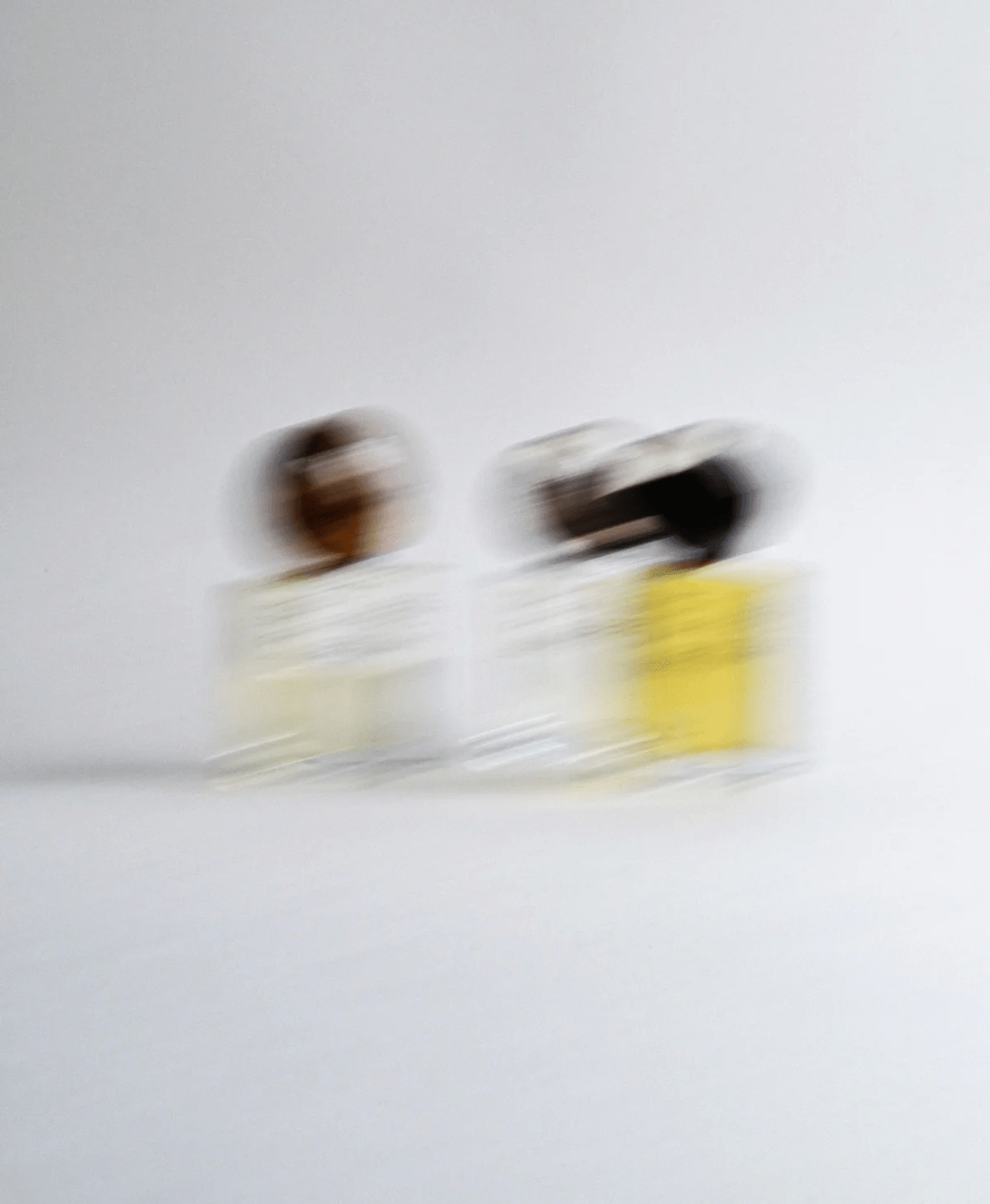 Blurry image of two glass bottles with yellow and brown liquid against grey background.