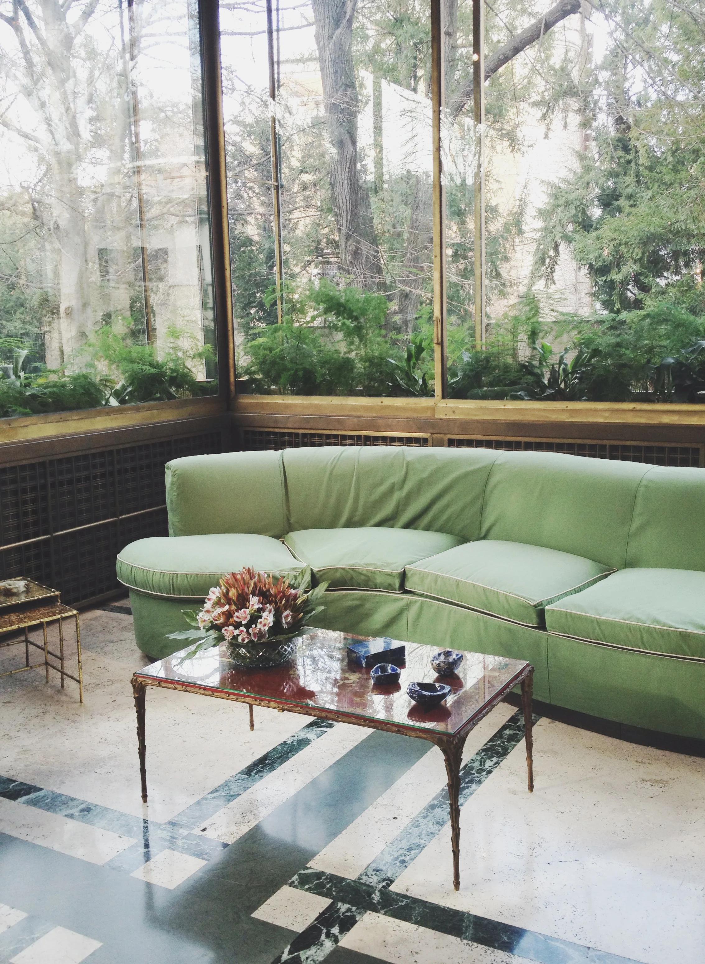 Cosy living room with garden view. Light green L-shaped sofa, wooden coffee table, and green-white tiled floor showcase R+D.LAB's design aesthetic.