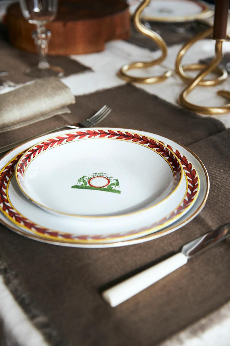 Two stacked plates with ornate designs, cutlery on brown napkin. Golden candlestick partially visible.