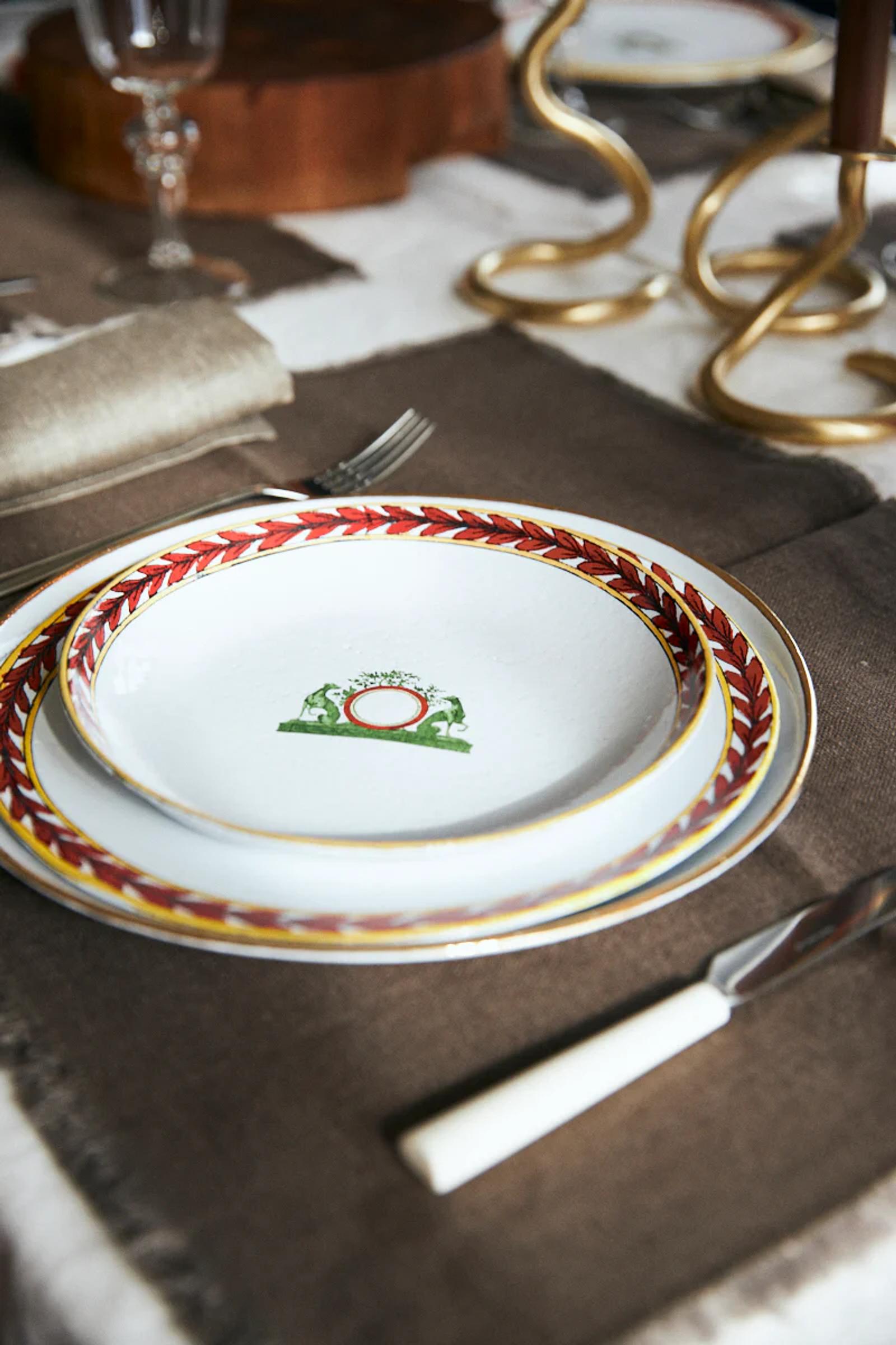 Two stacked plates with ornate designs, cutlery on brown napkin. Golden candlestick partially visible.