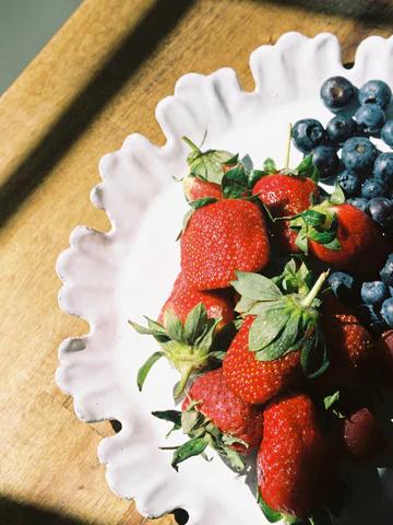 A white plate with fresh strawberries and blueberries on a wooden surface, illuminated by sunlight, perfect for festive celebrations.