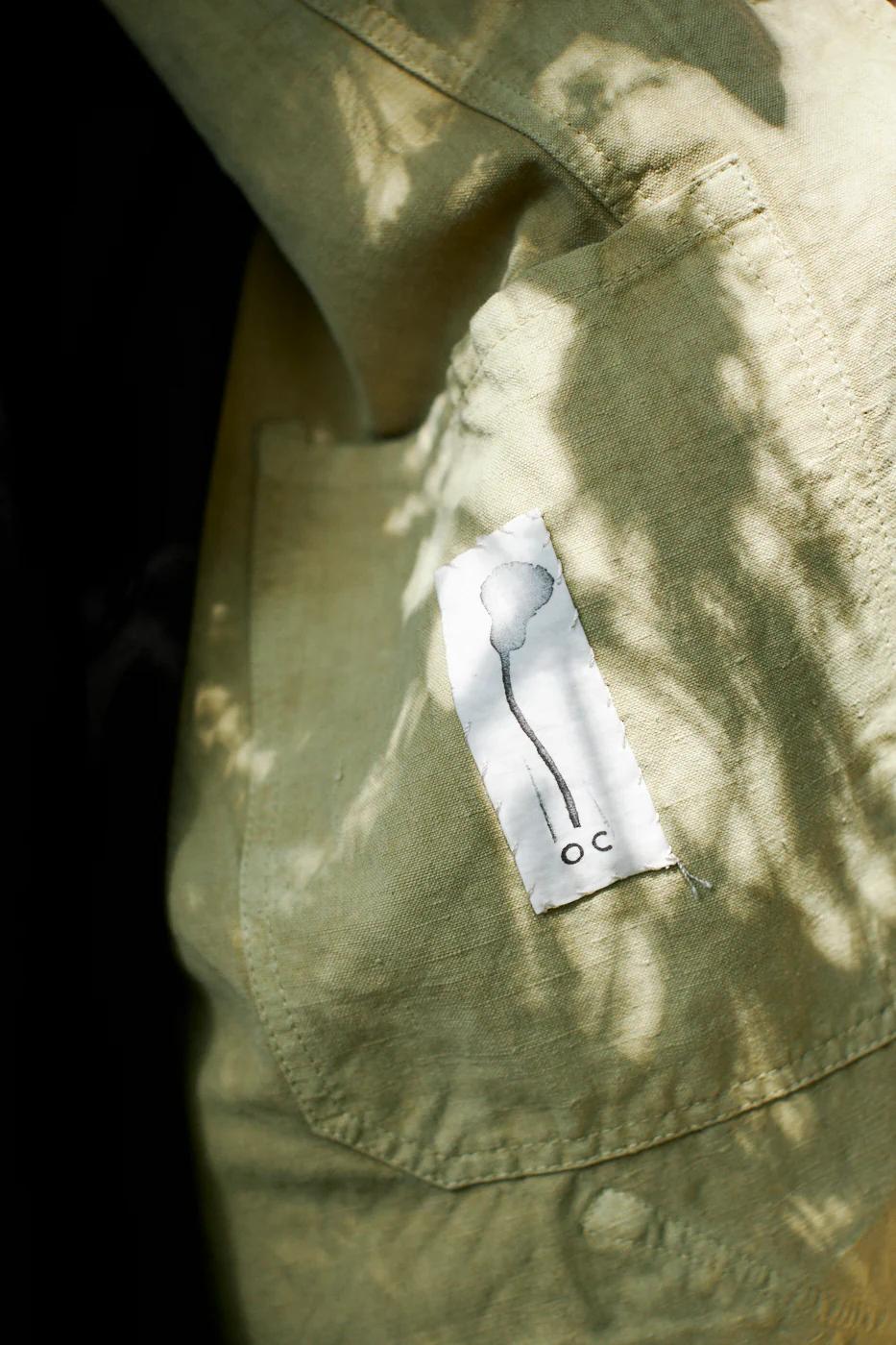 Green fabric with small label featuring upside-down tree drawing. Dappled sunlight on fabric.