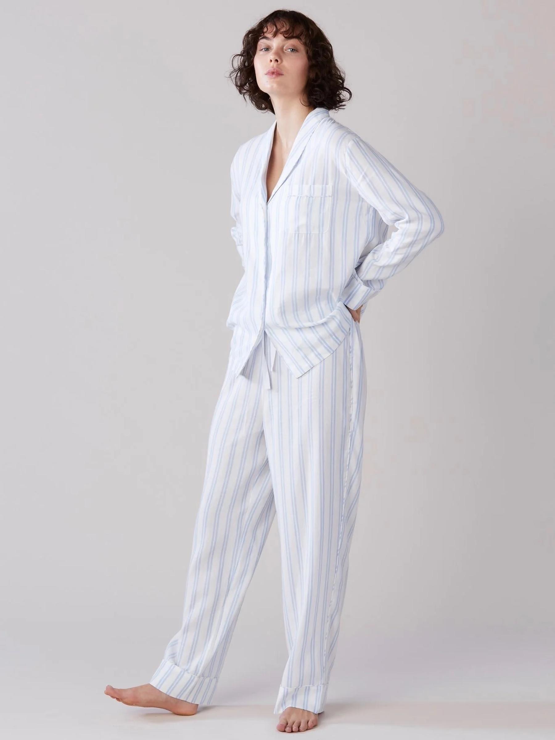 Close-up: Person wearing long dark gray ribbed cardigan and black pants. Hand in cardigan pocket. Plain light background.